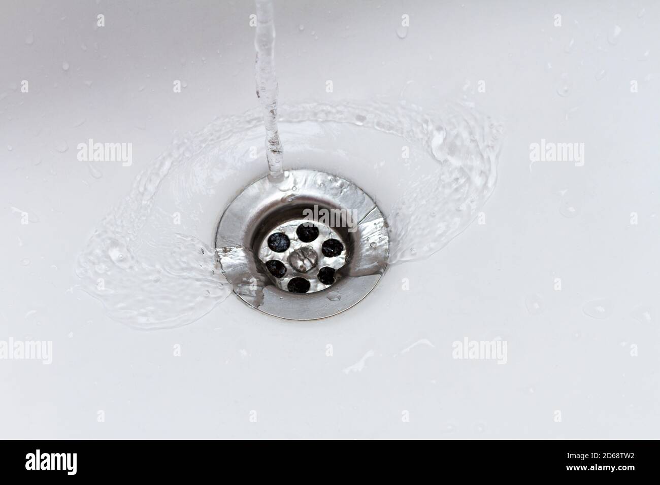Wasser fließt aus dem Wasserhahn in den Abfluss des Waschbeckens Stockfoto