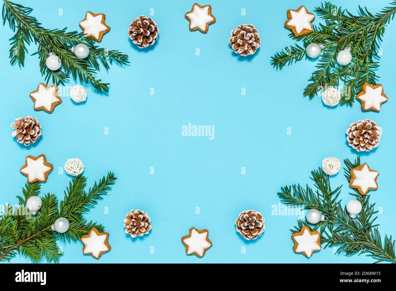 Weihnachtsrahmen mit Bio-Dekoration: Nadelbaum Äste, Tannenzapfen, Zimt-Sternkekse und Kugeln auf blauem Hintergrund Stockfoto