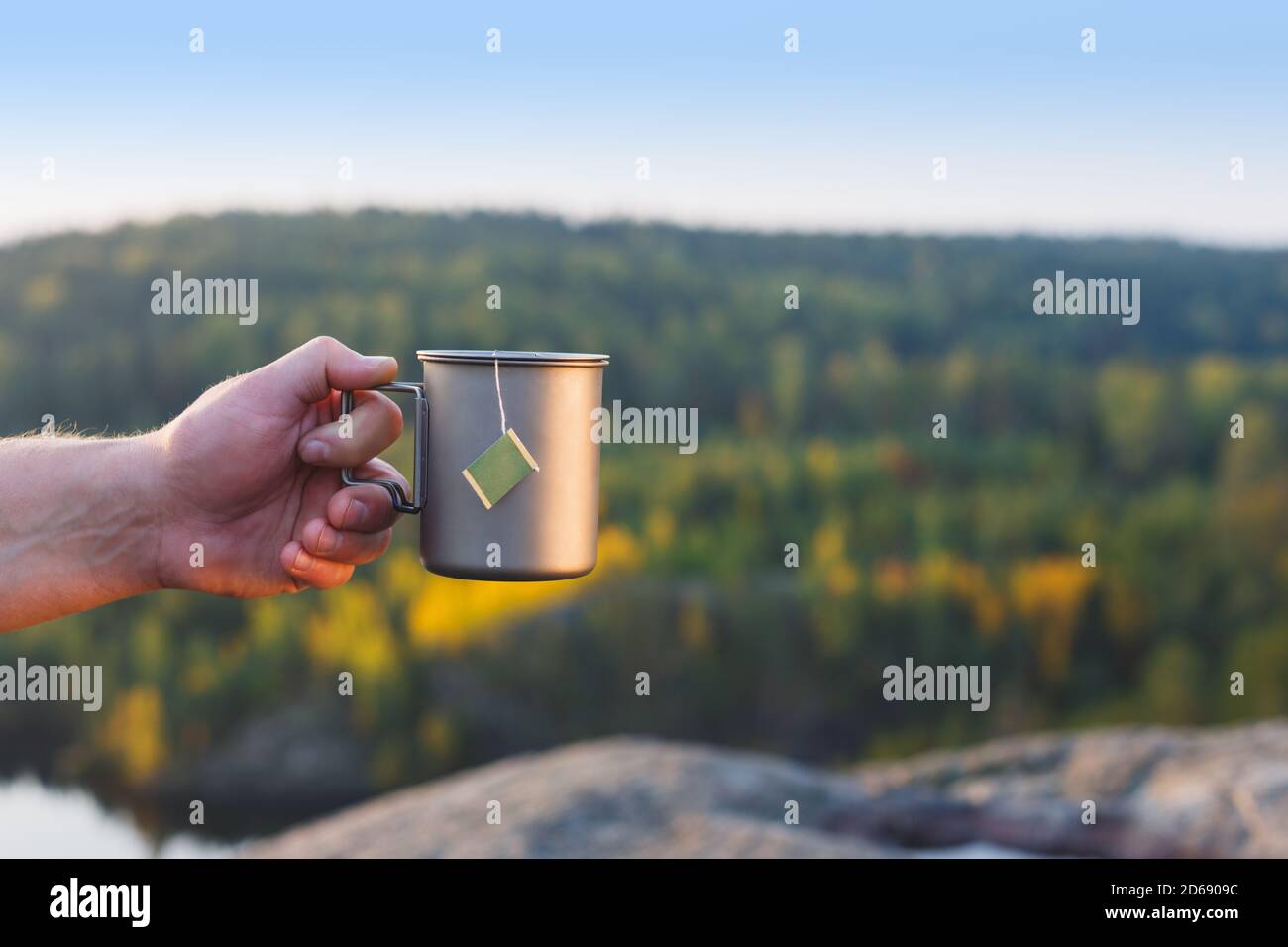 Ein Mann hält eine Tasse Tee in der Hand vor dem Hintergrund eines Herbstwaldes. Stockfoto