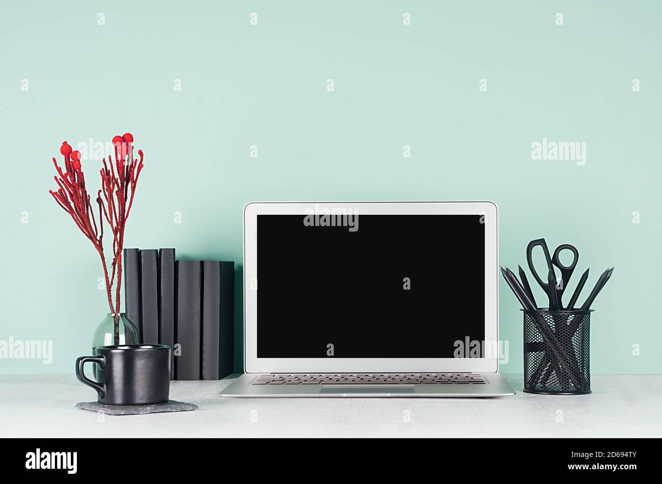 Frischer Arbeitsplatz für Bildung, Arbeit mit leerem Notebook-Bildschirm, schwarzer Schreibwaren, Bücher, Kaffeetasse, roter Deko-Zweig in grüner Minze menthe Interieur Stockfoto