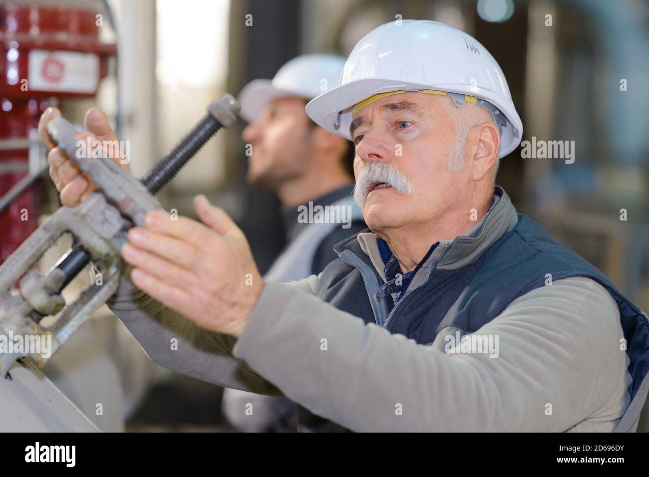 senio-Handarbeiter, der das Absperrventil im Werk dreht Stockfoto