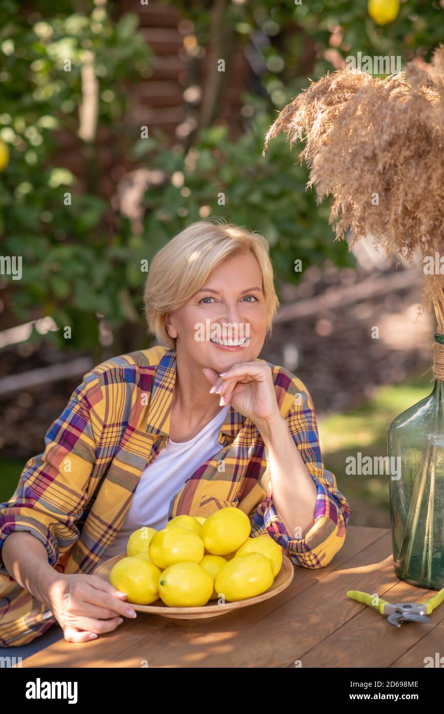Lächelnd blonde Frau sitzt am Tisch mit Teller Zitronen im Garten Stockfoto