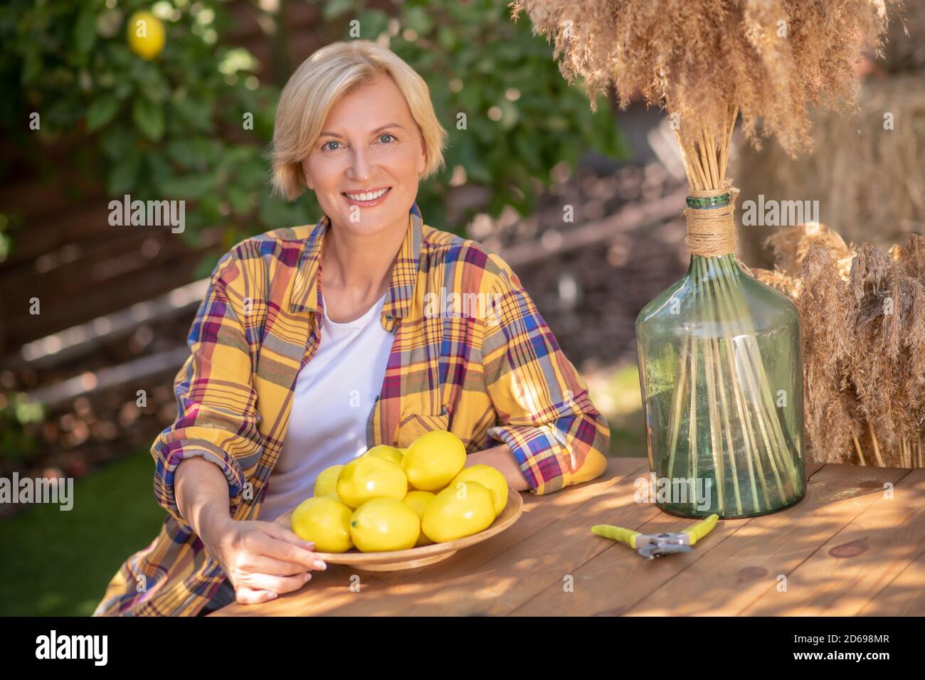Blonde Frau sitzt am Holztisch mit Teller Zitronen im Garten Stockfoto