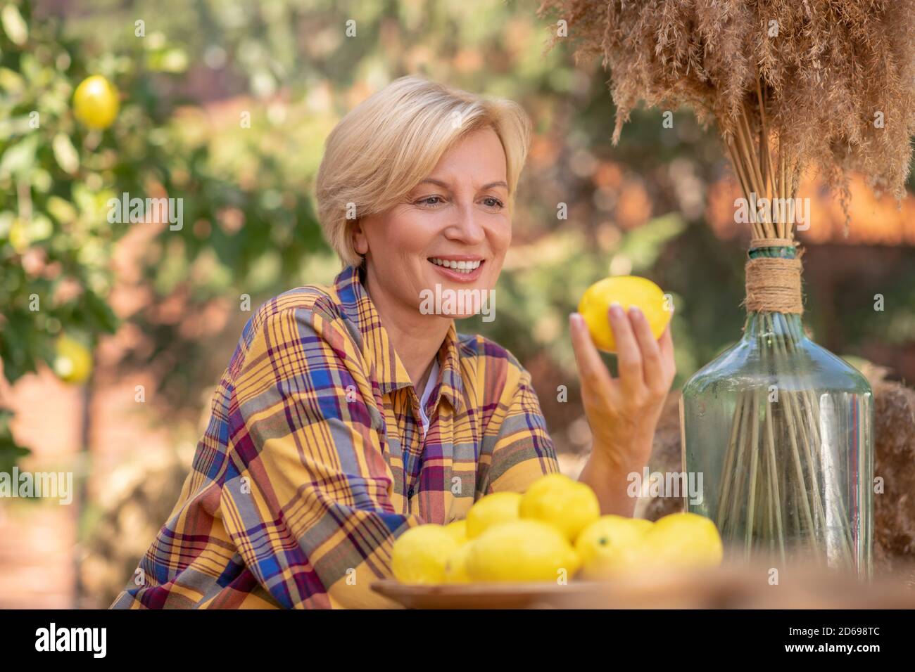 Blonde Frau sitzt am Holztisch im Garten, hält Zitrone Stockfoto