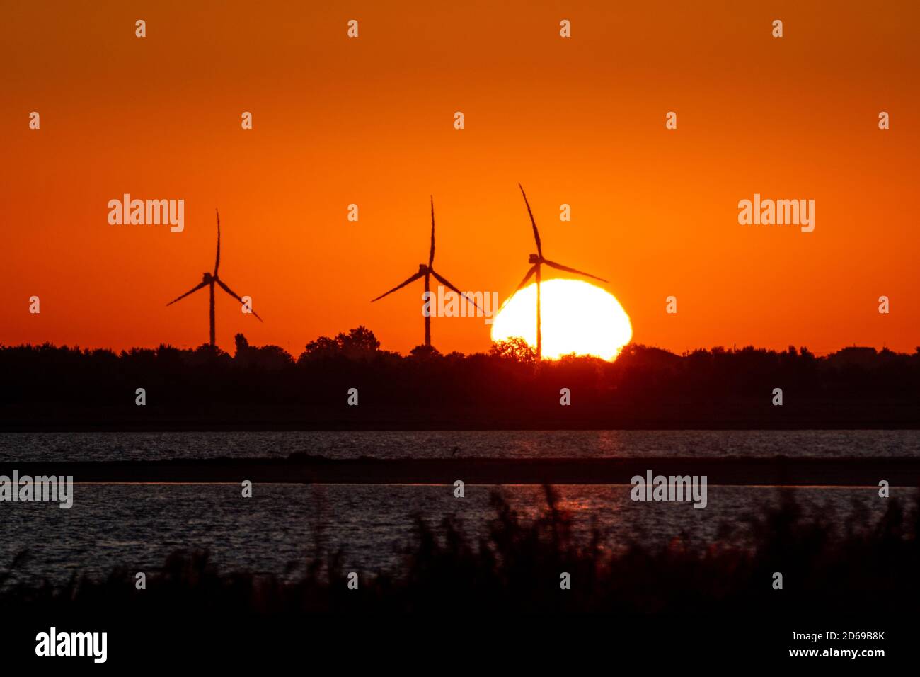 Windgeneratoren Farm Silhouette an der Küste im Sonnenaufgang rot orange vibrierenden Himmel und große aufgehende Sonne. Energieturbinen nachhaltige Industrie Stockfoto