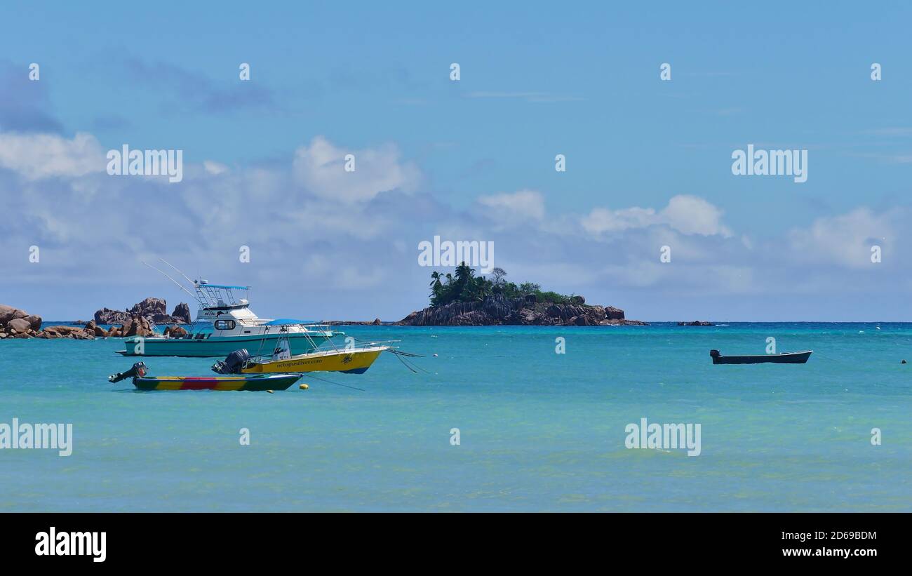 Anse Volbert, Praslin, Seychellen - 09/25/2018: Boote, die in türkisfarbenem Meer am tropischen Strand Anse Volbert mit kleiner Insel St. Pierre anlegen. Stockfoto