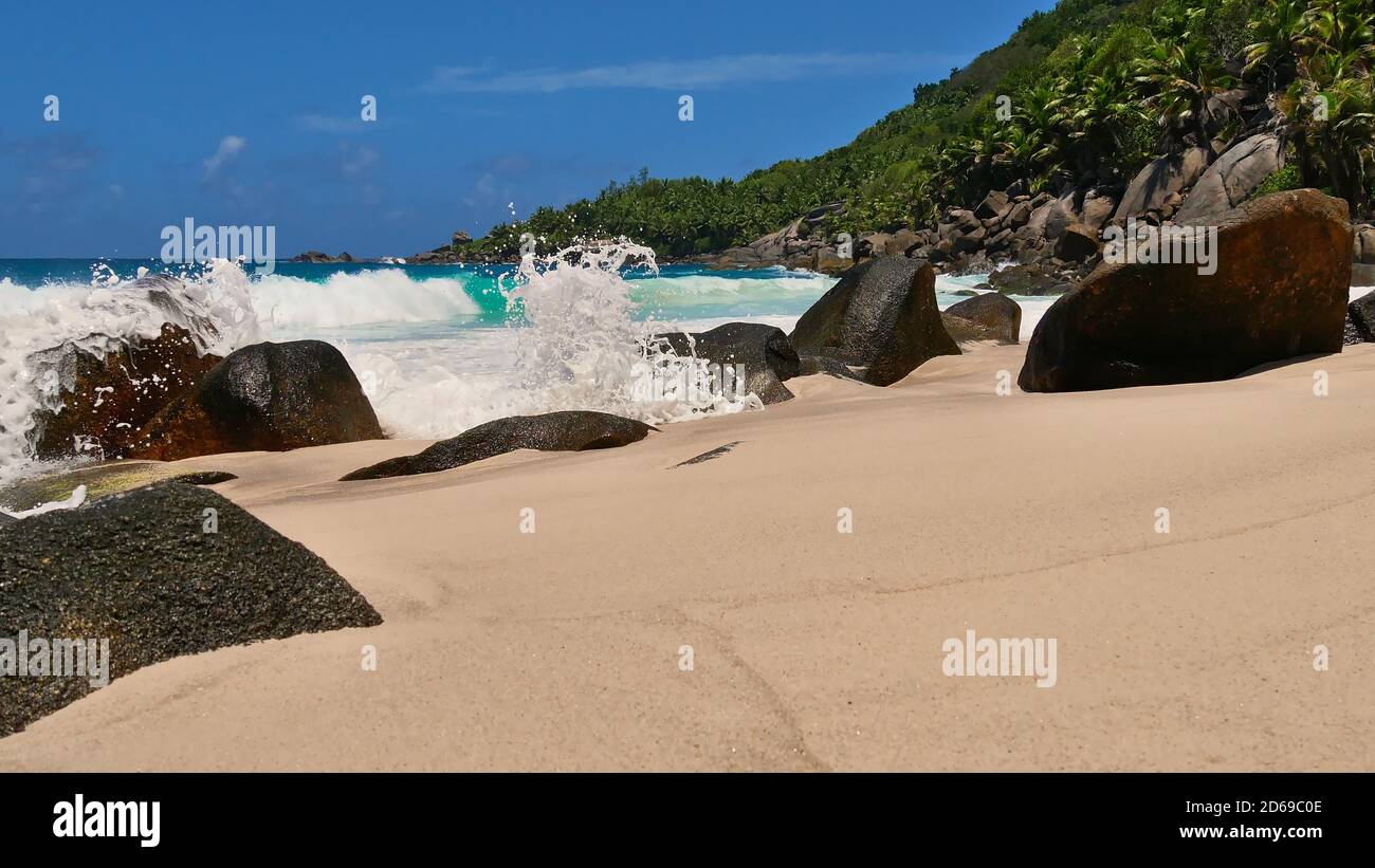 Starke Wellen schlagen gegen Granitfelsen mit Spray und Schaum am abgelegenen tropischen Strand Anse Capucins, Mahe Island, Seychellen. Stockfoto