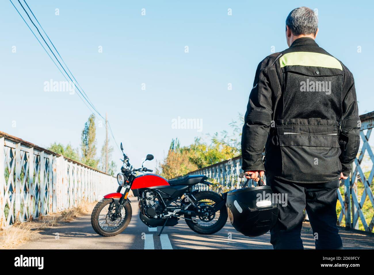 Mann auf dem Rücken, der ein Motorrad mit einem anschaut Helm in der Hand Stockfoto