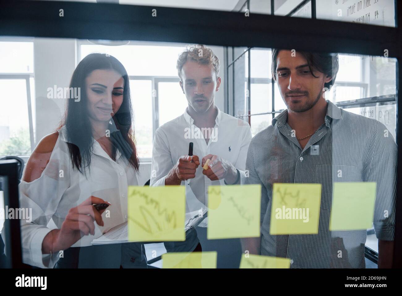 Gelbe Aufkleber sind auf dem Glas. Junge Geschäftsleute in formeller Kleidung arbeiten im Büro Stockfoto