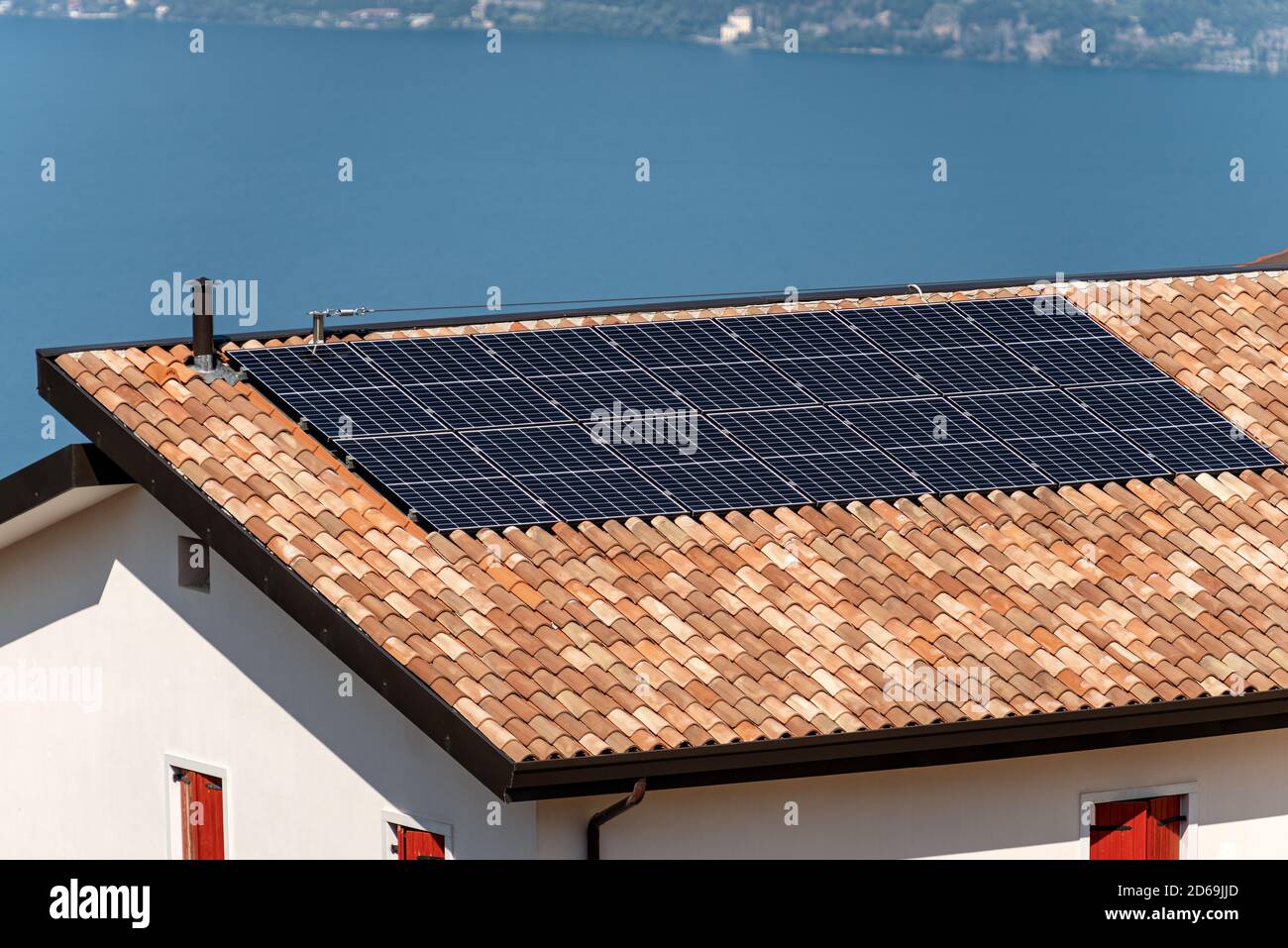 Sonnenkollektoren auf dem Dach eines Hauses mit einem blauen See im Hintergrund. Konzept für erneuerbare Energien Stockfoto