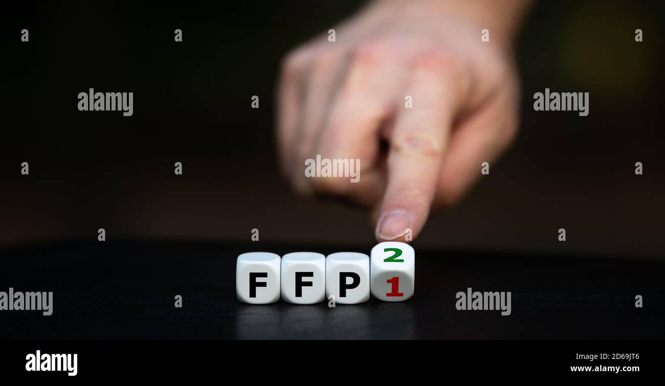 Symbol für das Tragen einer FFP2-Maske. Hand dreht Würfel und ändert den Ausdruck 'FFP1' in 'FFP2'. Stockfoto