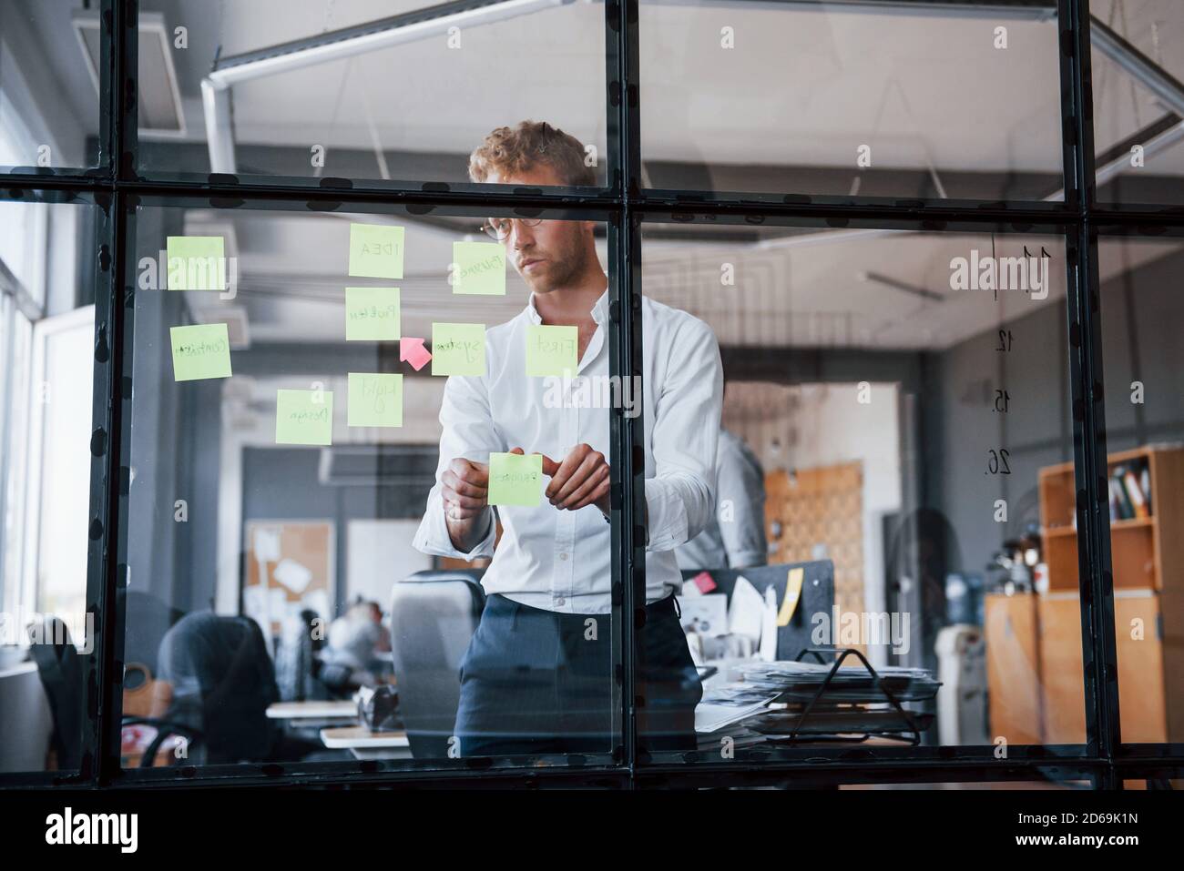Mann in formeller Kleidung steht im Büro hinter dem Glas und setzt Aufkleber darauf Stockfoto