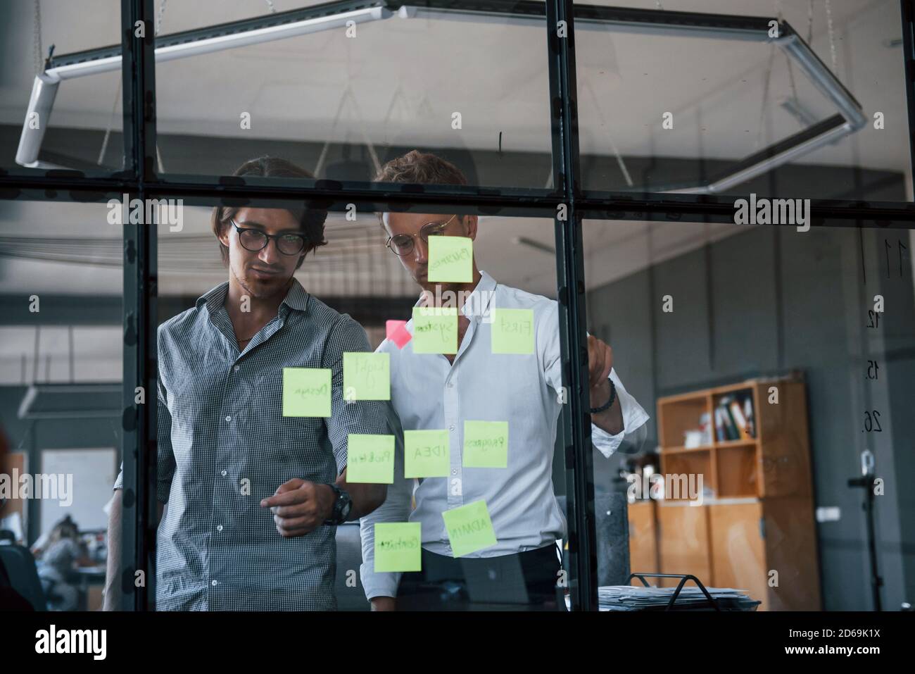 Zwei Jungs in formeller Kleidung steht im Büro dahinter Das Glas und setzt Aufkleber darauf Stockfoto