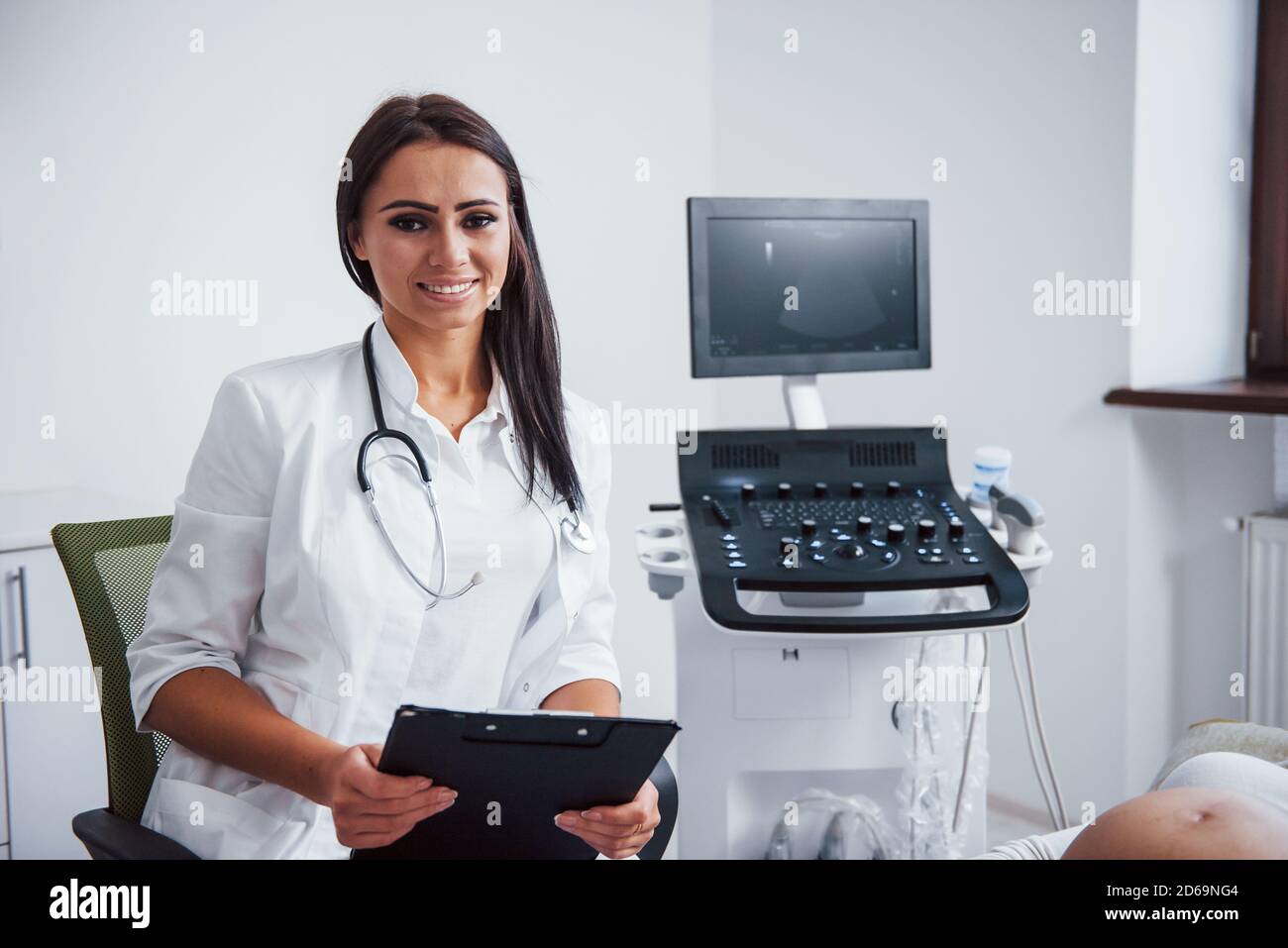 Portrait des Geburtsarztes, der im Klinikraum sitzt Mit Ultraschallgerät Stockfoto