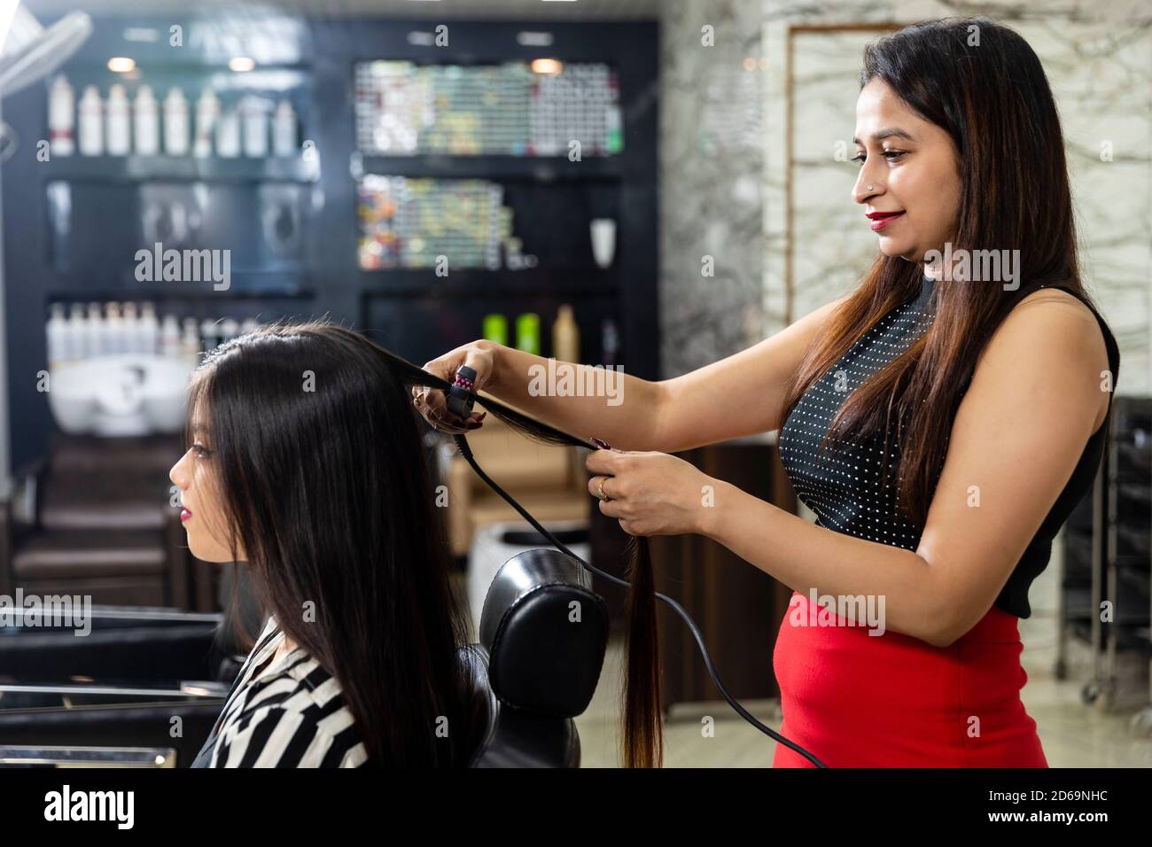 Ein Friseur bietet Haar Styling-Dienstleistungen für eine hübsche junge indische Frau, schöne Frau bekommt ihr Haar in einem Salon, selektive Fokus getan. Stockfoto