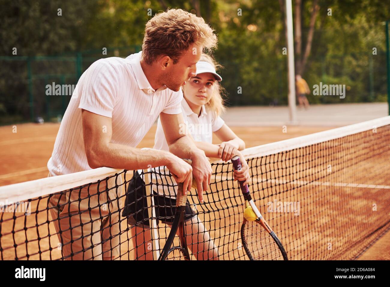 Eine Pause machen, indem man sich auf das Netz lehnt. Zwei Personen in Sportuniform spielen gemeinsam Tennis auf dem Platz Stockfoto