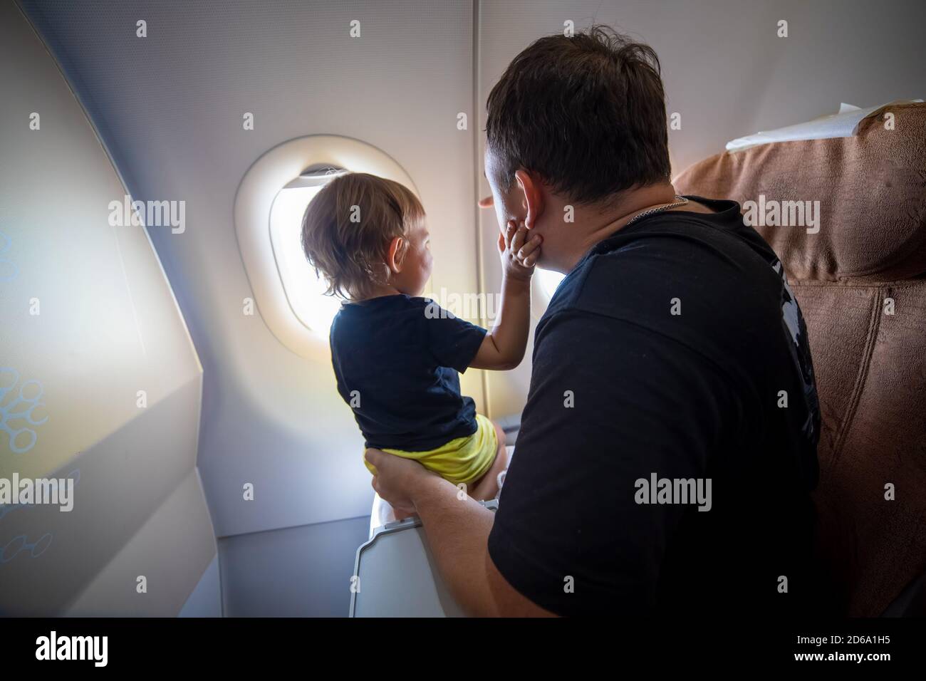 Vater und niedliche Kleinkind sitzen auf einem Flugzeug und Blick in den Himmel durch das Bullauge. First Flight Konzept, Reisen mit Kindern Stockfoto