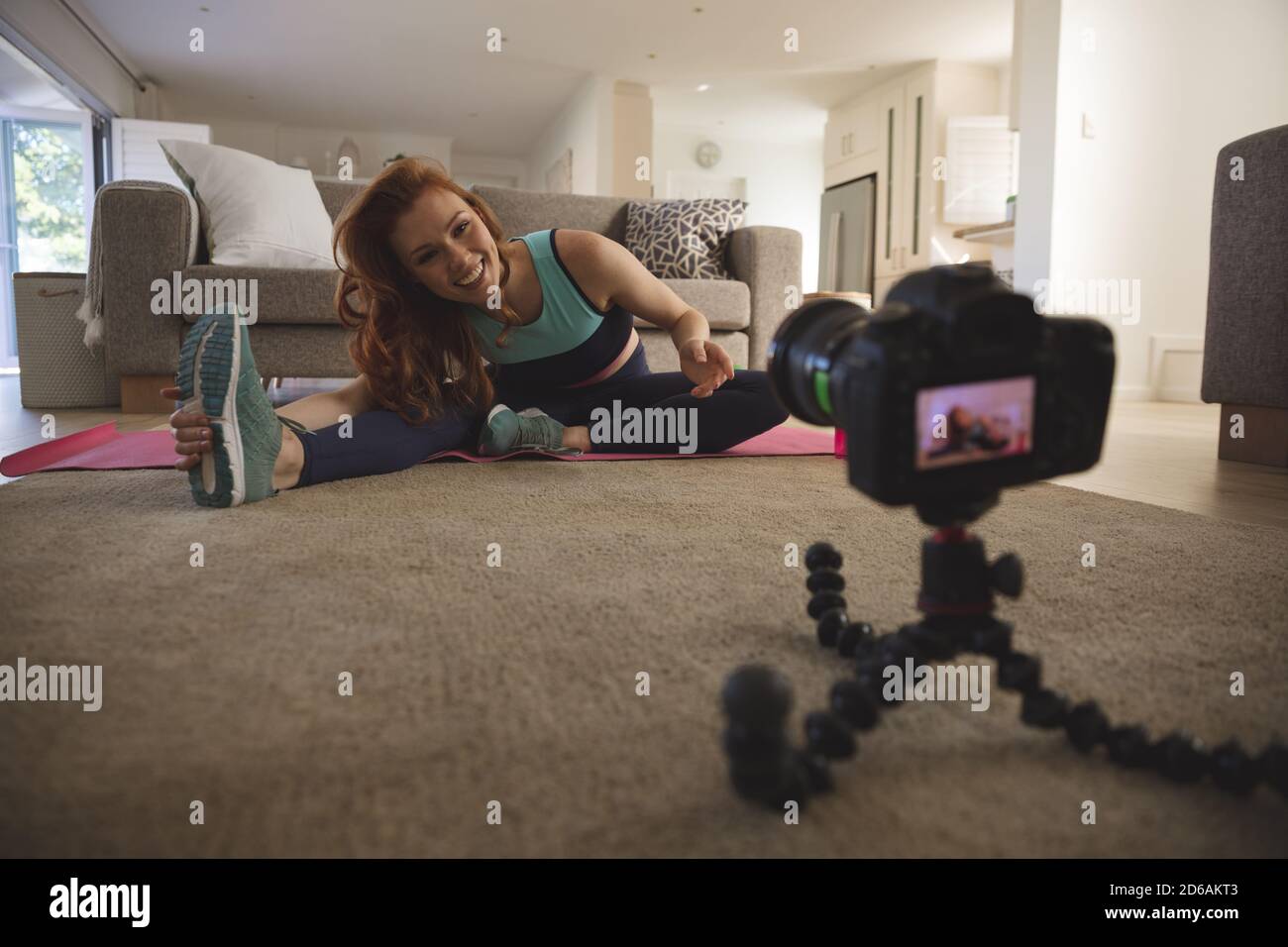 Frau, die Stretching-Übung beim Blick auf Digitalkamera an Zu Hause Stockfoto