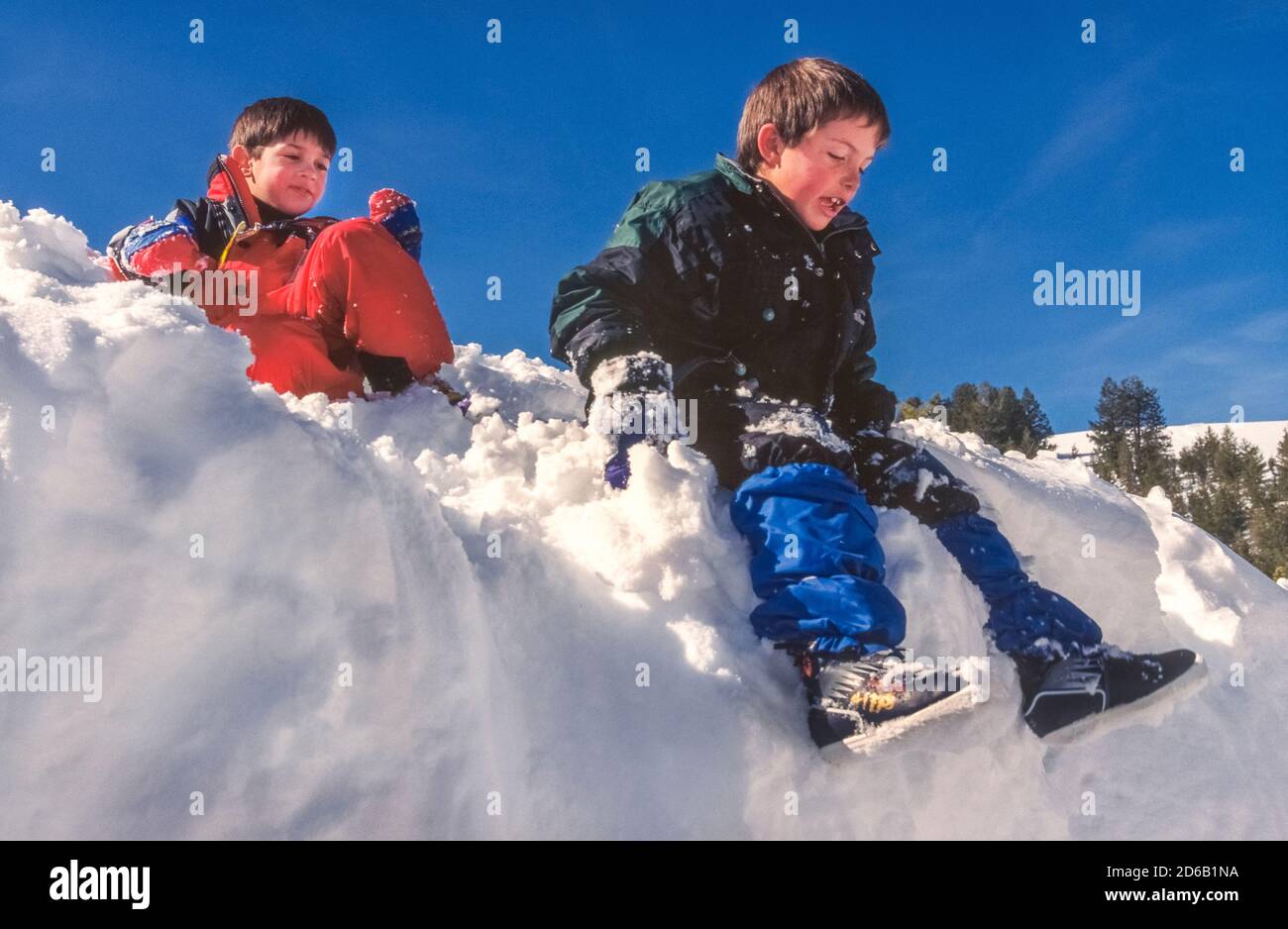 Zwei junge amerikanische Jungs haben Spaß, an einem sonnigen Wintertag in den Sawtooth Mountains in Idaho, USA, über einen Schneedamm zu gleiten. Im Winter ist das Sawtooth National Recreation Area ein riesiger verschneit Spielplatz mit Meilen von Wegen für Langlauf, Schneeschuhwandern und Motorschlittenfahrten. Stockfoto