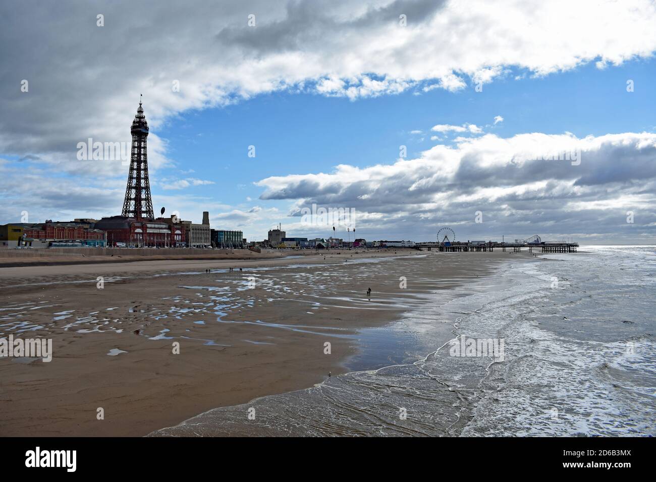 Blick entlang Blackpool Strand von North Pier zum Central Pier. Der Blackpool Tower steht hoch an der Promenade. Besucher spazieren am Strand entlang, England Stockfoto