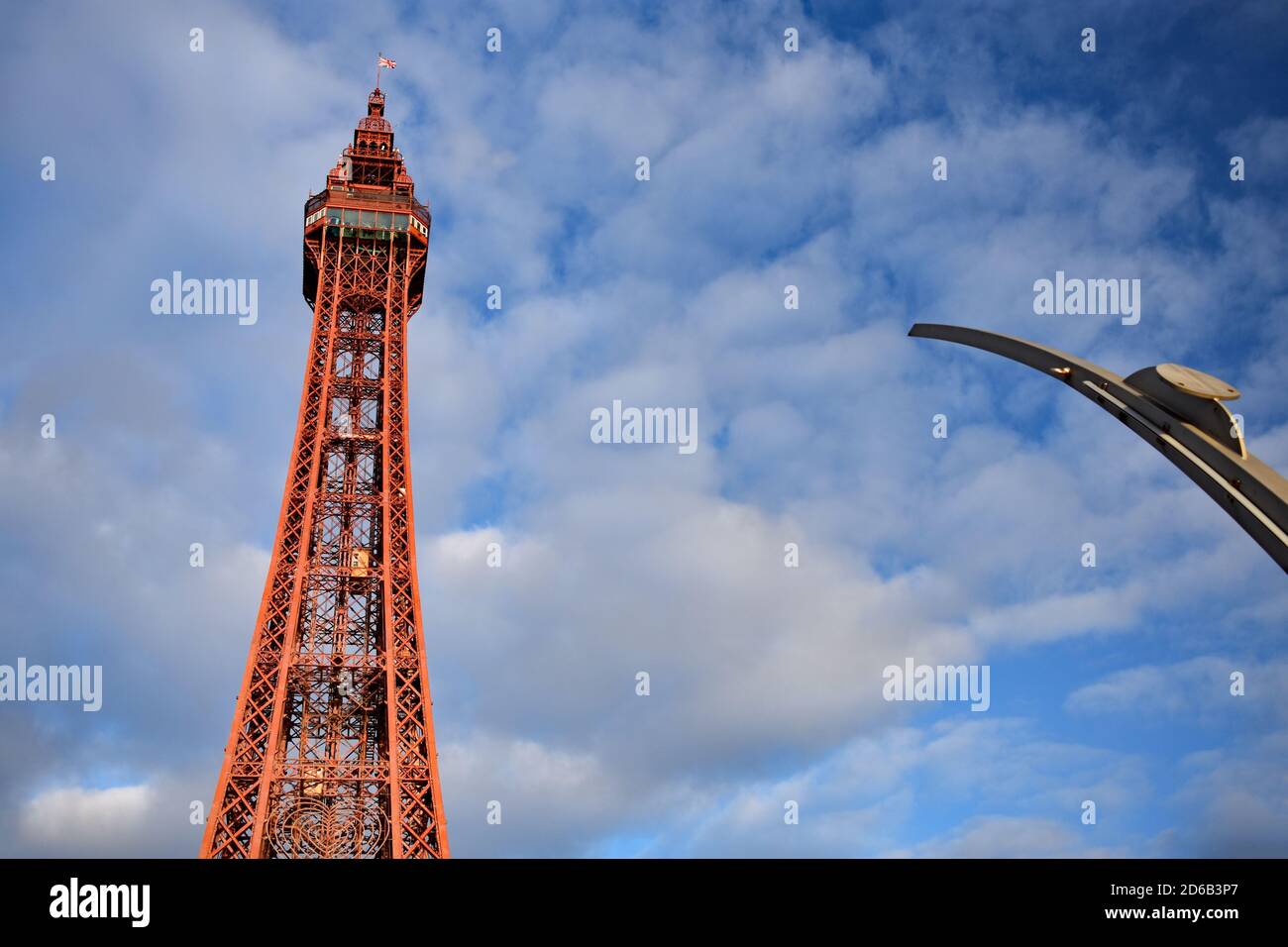 Von der Promenade aus blickt man nach oben auf den dunkelroten Blackpool Tower, während die Sonne durch die Wolken bricht, Lancashire, England. Stockfoto