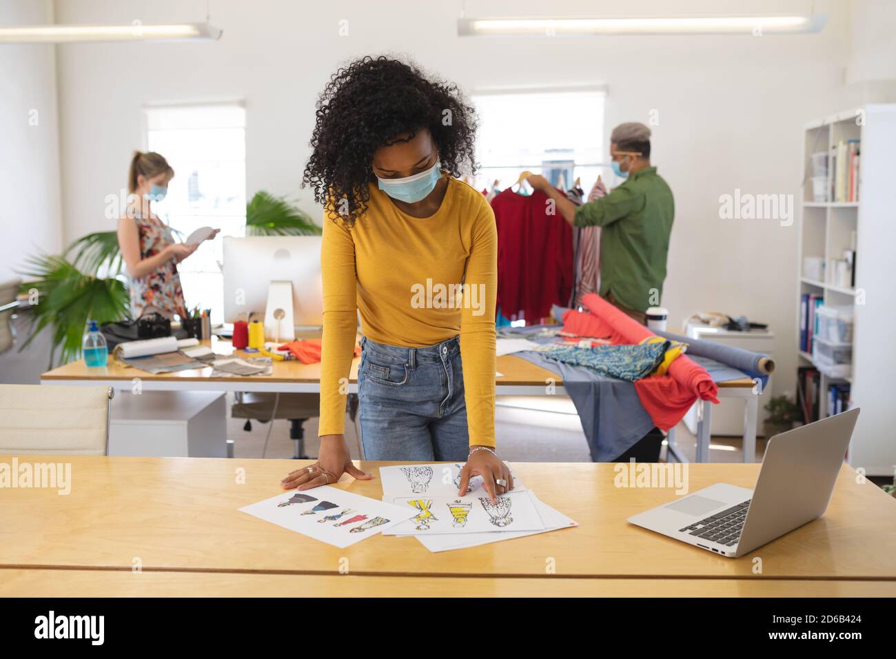 Weibliche Modedesignerin trägt Gesichtsmaske Blick auf Skizzen Bekleidungsdesign im Studio Stockfoto