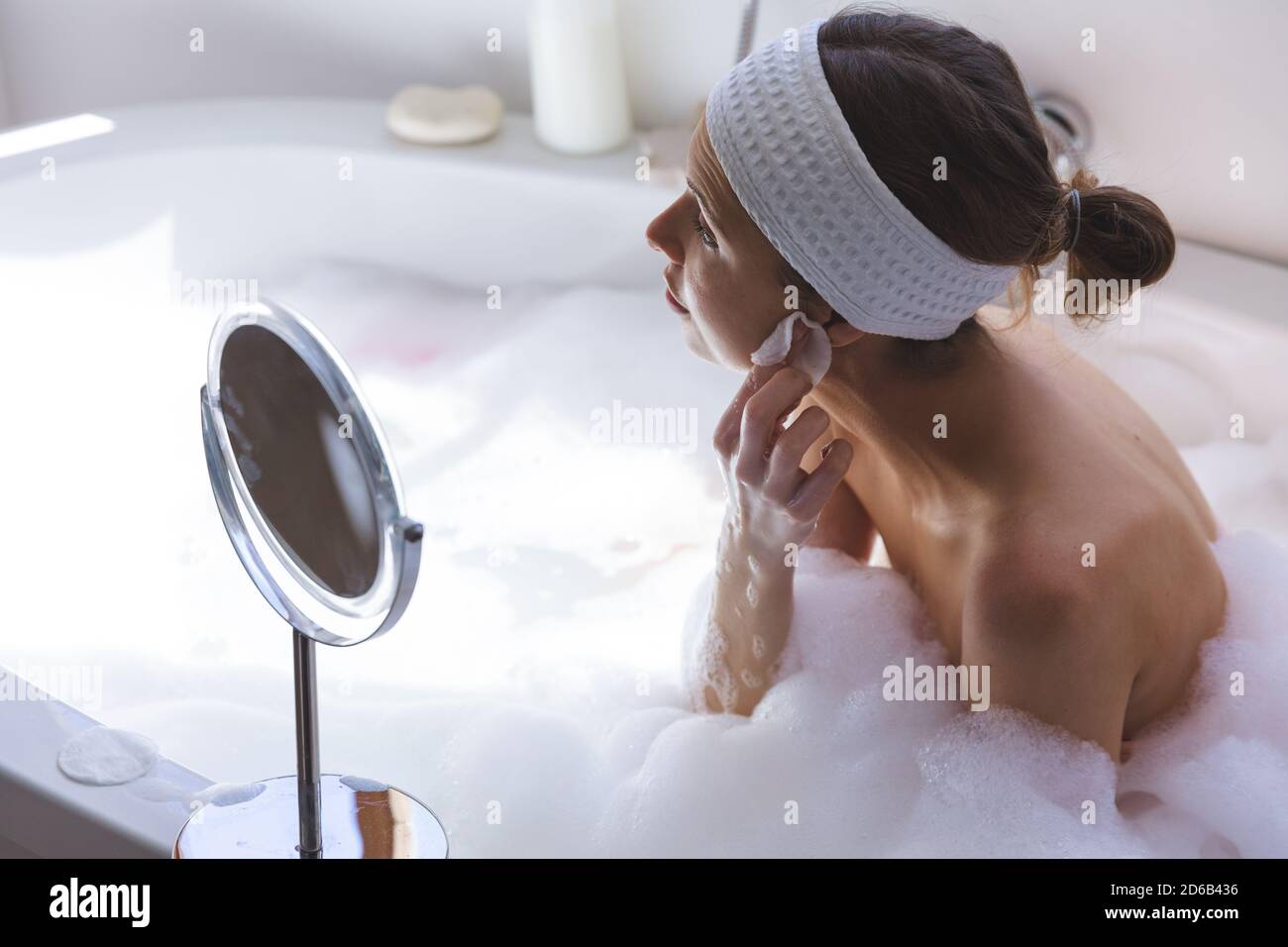 Frau, die ihr Gesicht mit Wattepad reinigt, während sie im Sitzen sitzt Badewanne Stockfoto