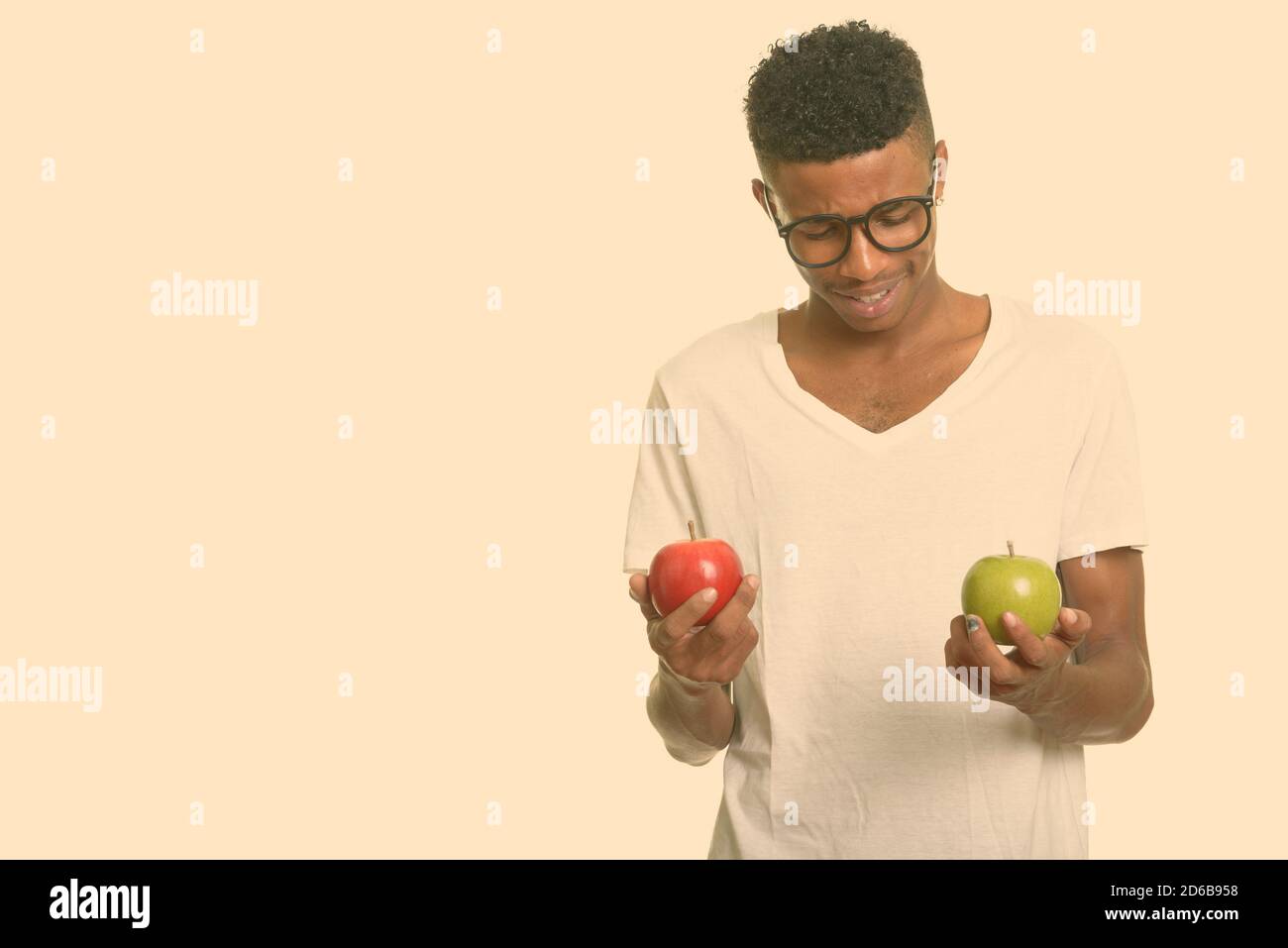 Junger glücklicher afrikanischer Mann, der zwischen rotem und grünem Apfel wählt Stockfoto