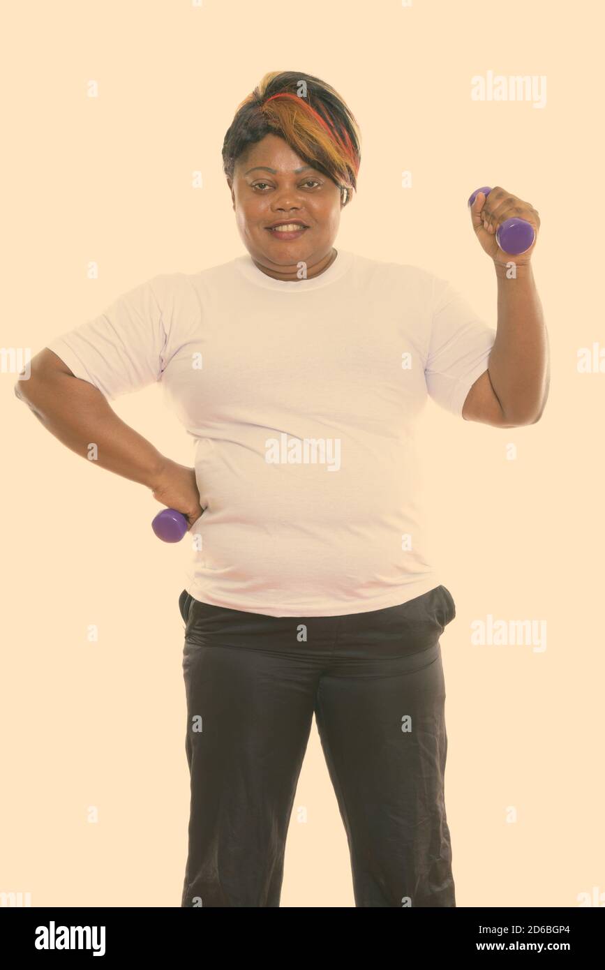 Studio Schuss von glücklich Fett schwarz afrikanische Frau lächelnd und Stehen mit Hanteln in beiden Händen bereit für das Fitnessstudio Stockfoto