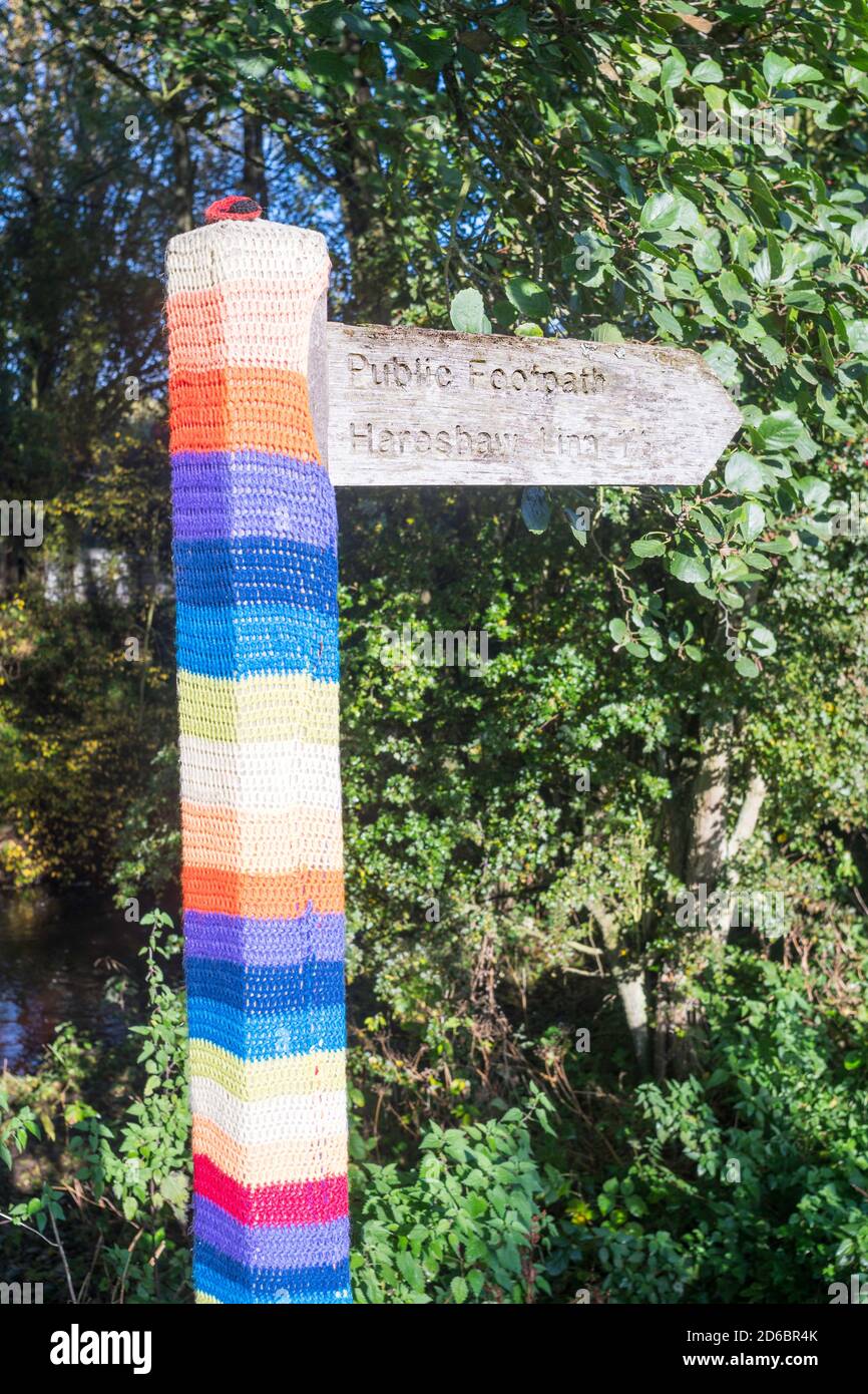 Holzschild mit NHS Regenbogen gestrickt Abdeckung zeigt auf Hareshaw Linn Wasserfall in der Nähe von Bellingham in Northumberland, England, UK Stockfoto