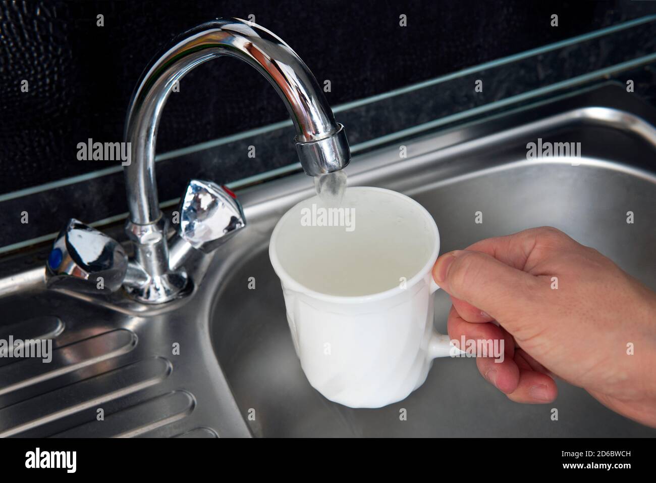 Sauberes gefiltertes Wasser fließt aus dem Wasserhahn. Gefahr von unbehandeltem Trinkwasser. Befüllen von Wasser in weißem Porzellanglas am Spülbecken Stockfoto