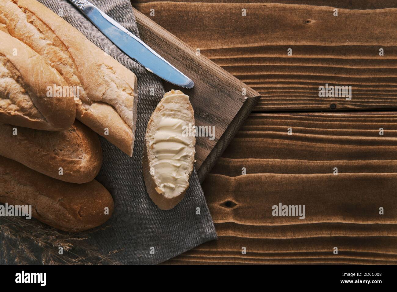 Draufsicht frisch geschnittenes französisches Baguette mit Butter auf A Leinentuch mit Messer auf einem Holztisch Stockfoto