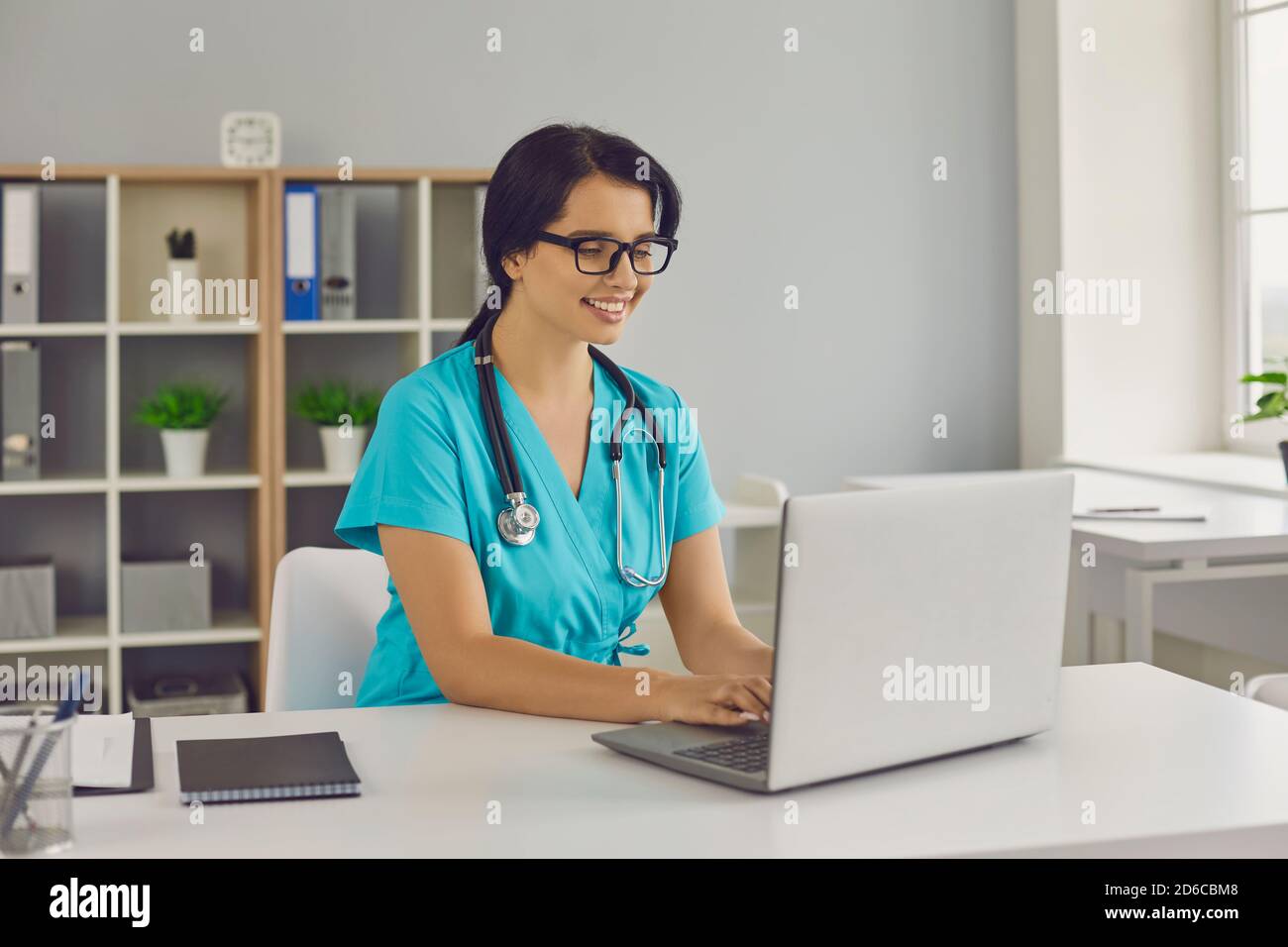 Junge lächelnde Arzt sitzen und arbeiten auf Laptop online in Medizinische Klinik Stockfoto