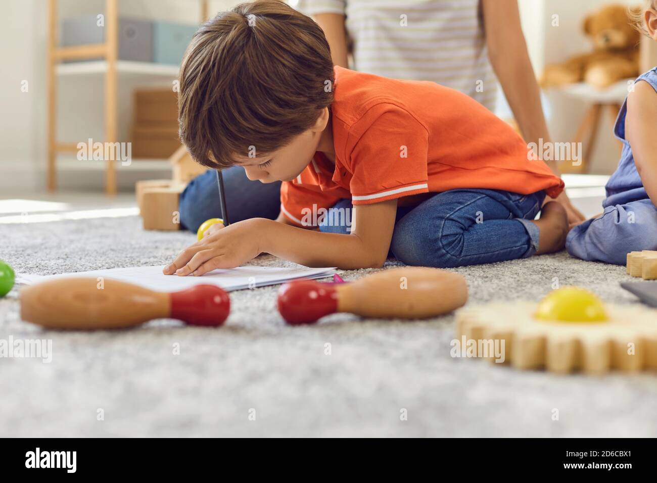 Vorschulkinder zeichnen ein Bild mit Bleistiften sitzen auf warmen Teppich Mit seinem Bruder und Kindermädchen Stockfoto