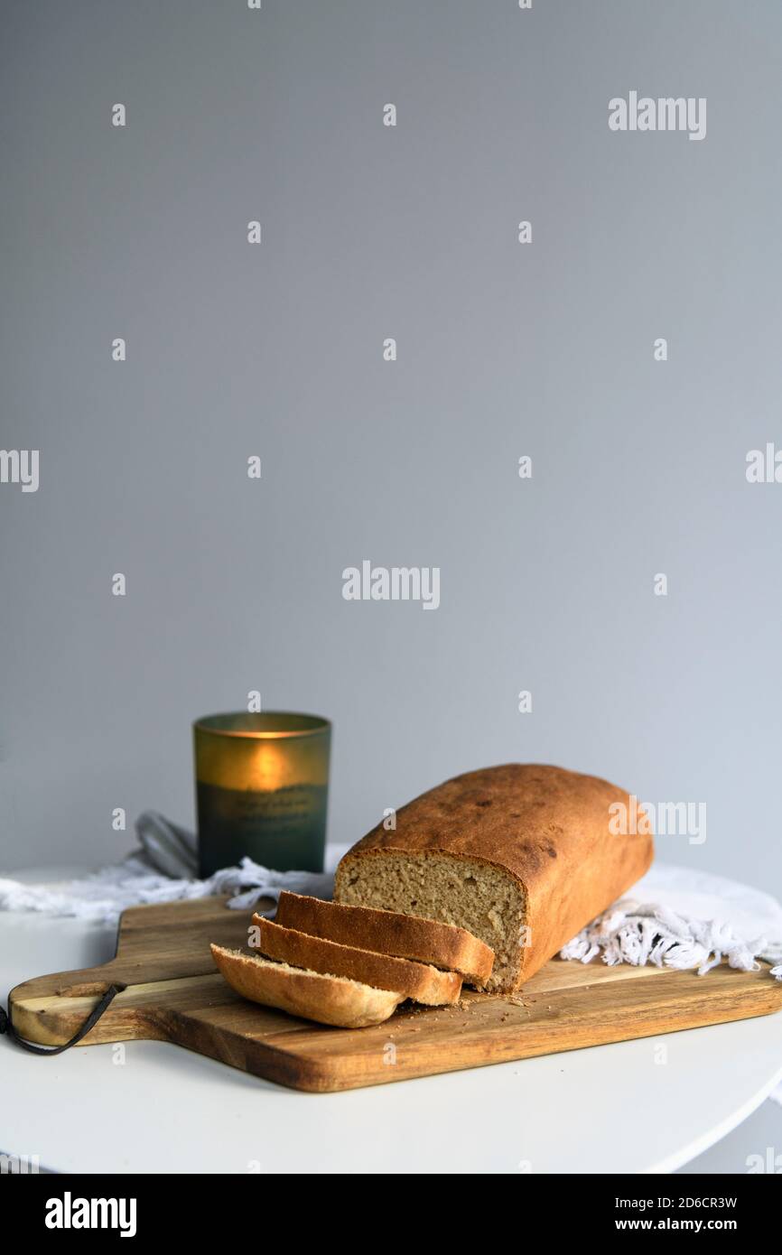 Hausgemachtes Brot in Scheiben auf einem Holzbrett mit einem Kerze auf einer weißen Serviette Stockfoto