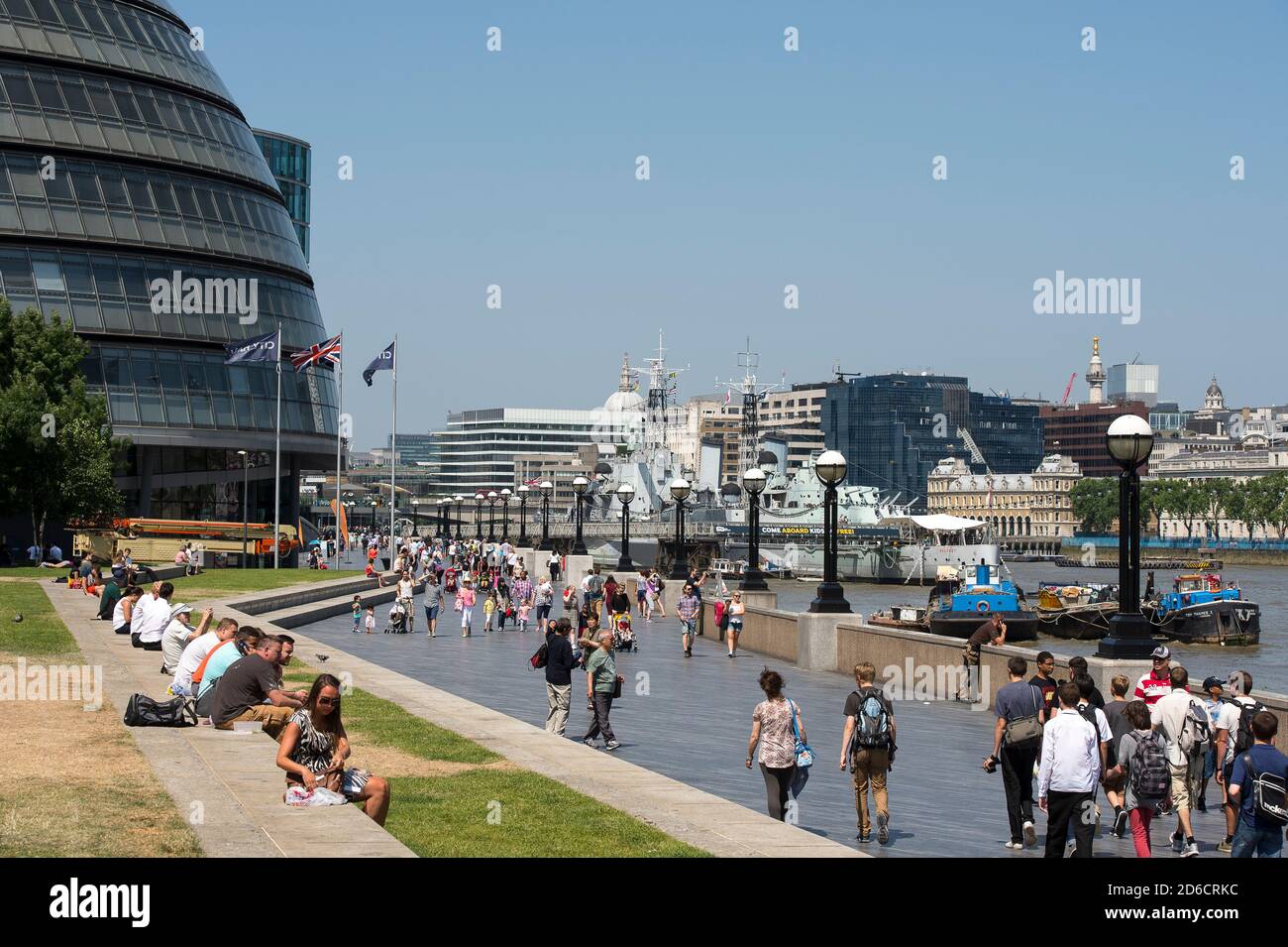 Touristen, die am Südufer der Themse mit der HMS Belfast und dem City Hall im Hintergrund, London, England, spazieren. Stockfoto