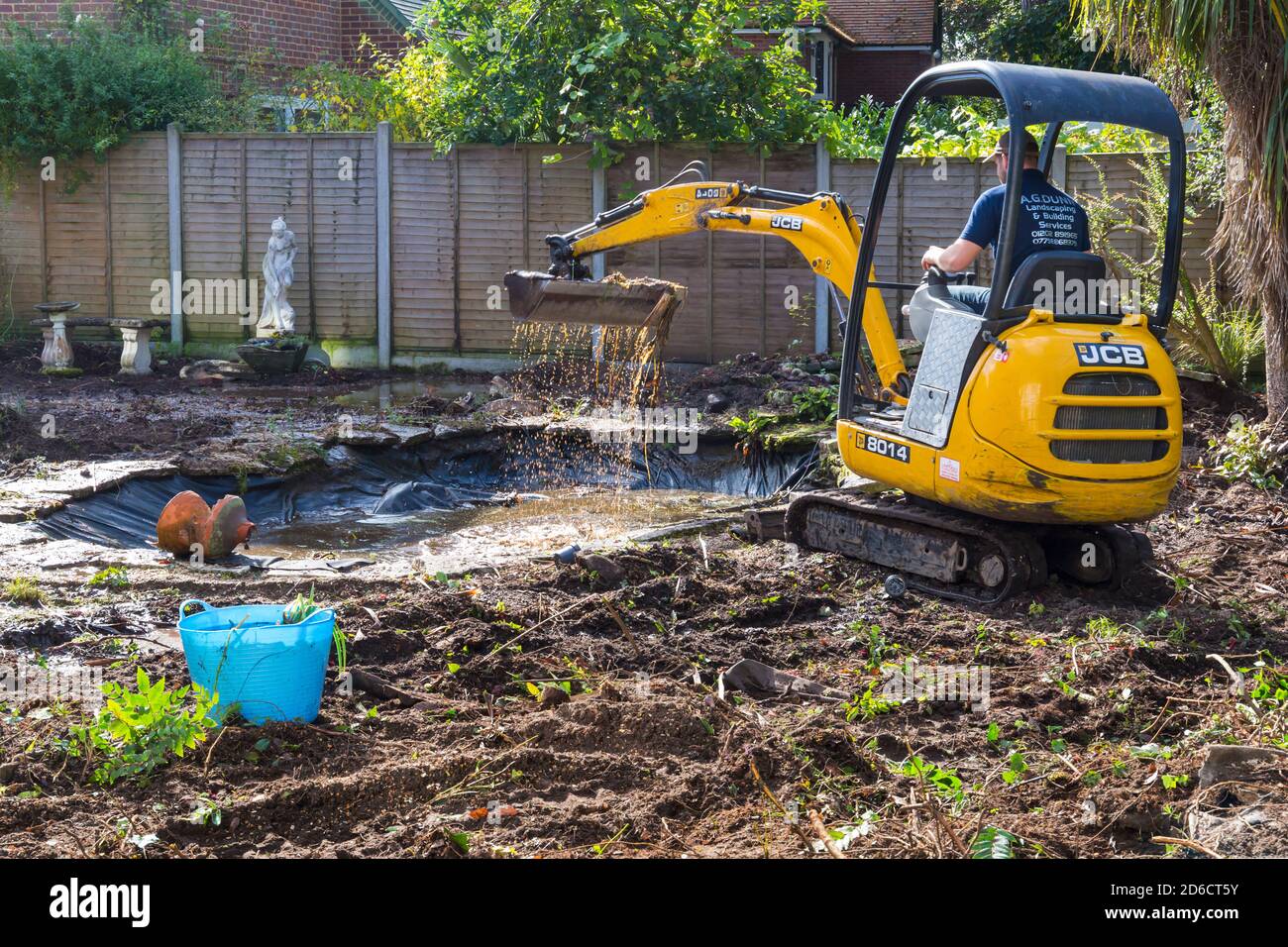 Gartenabräumarbeiten und Renovierungen, die im Oktober im Garten in Bournemouth, Dorset UK, stattfinden - Rodung des Gartenteiches mit jcb-Minibagger Stockfoto