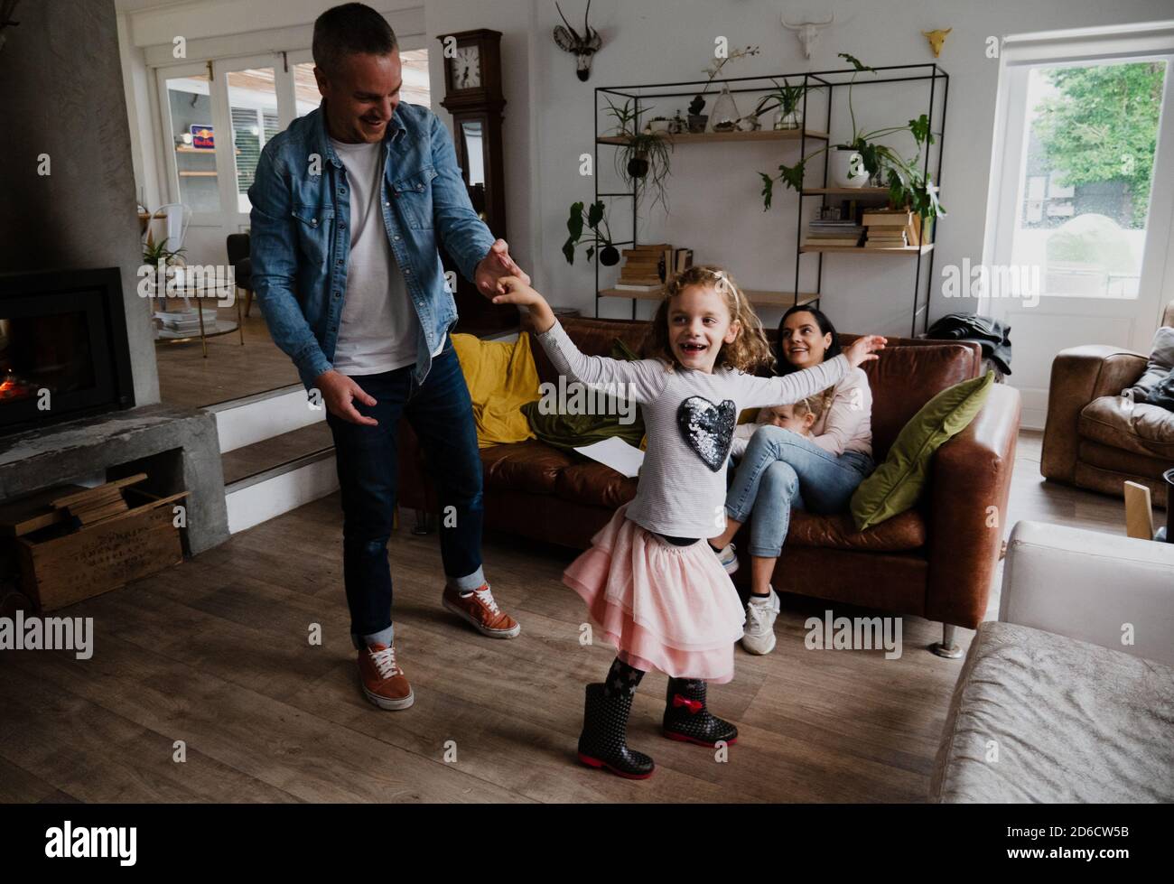 Vater und Tochter tanzen glücklich zusammen, während Mutter bequem sitzt Auf Wohnzimmer Sofa Stockfoto