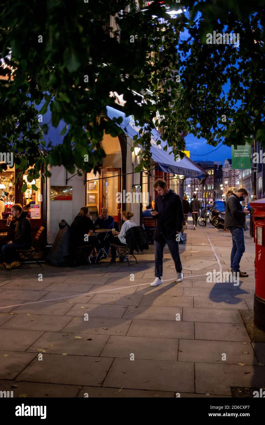 Die Kunden genießen ein gesellschaftlich distanziertes Getränk und ein Plauderei an Tischen auf der Straße vor einem öffentlichen Haus im West End in Londons Covent Garden. Wie viele Roa Stockfoto