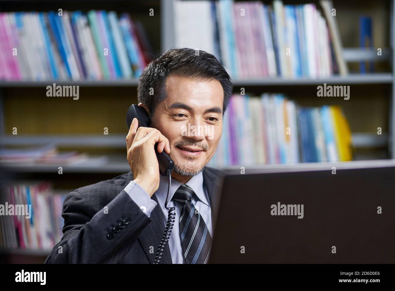 asiatischer Geschäftsführer sitzt im Büro am Schreibtisch und unterhält sich Telefon Stockfoto