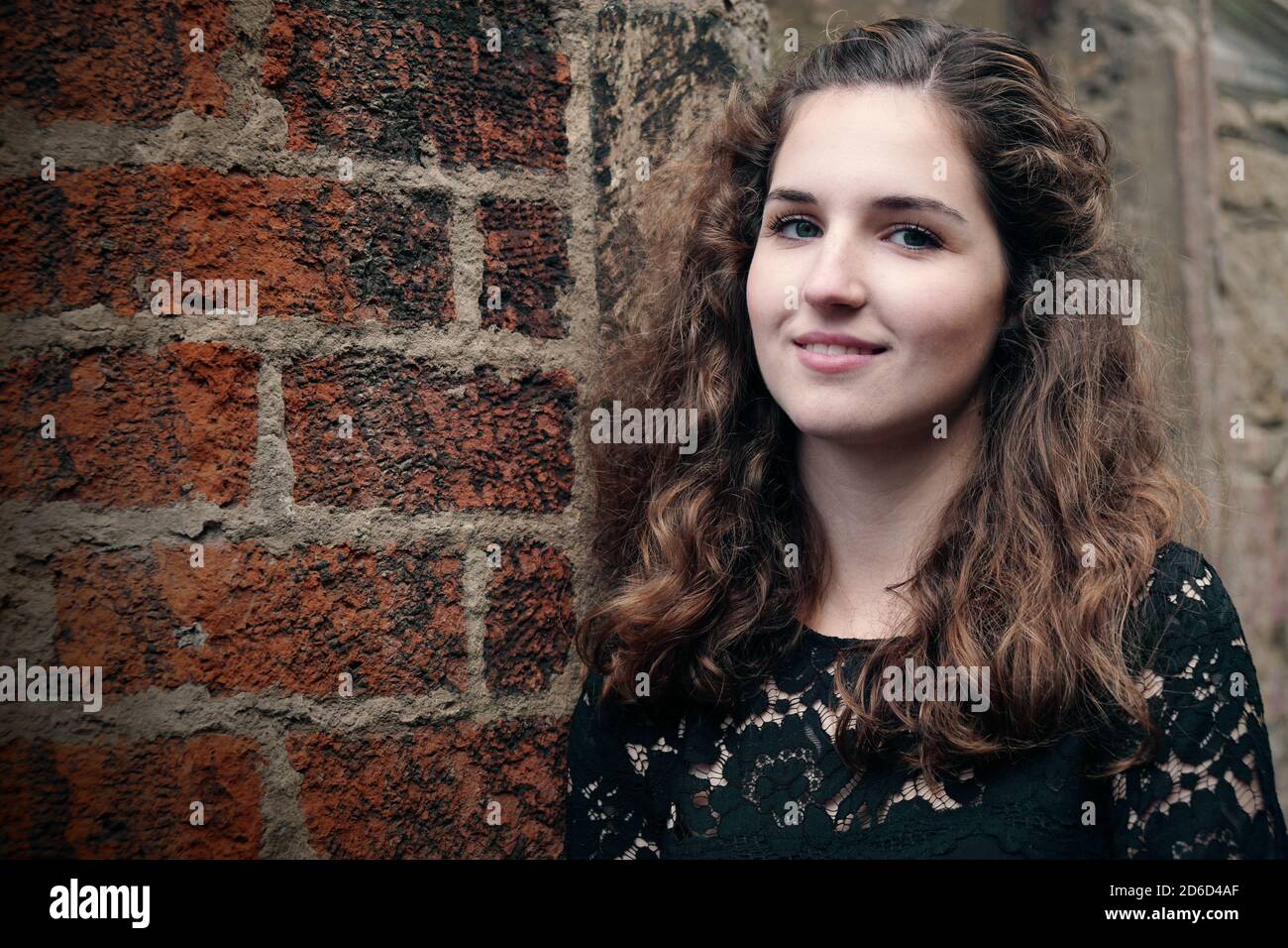 Glücklich lächelnde junge Frau lehnt an alte Backsteinmauer mit Speicherplatz kopieren Stockfoto