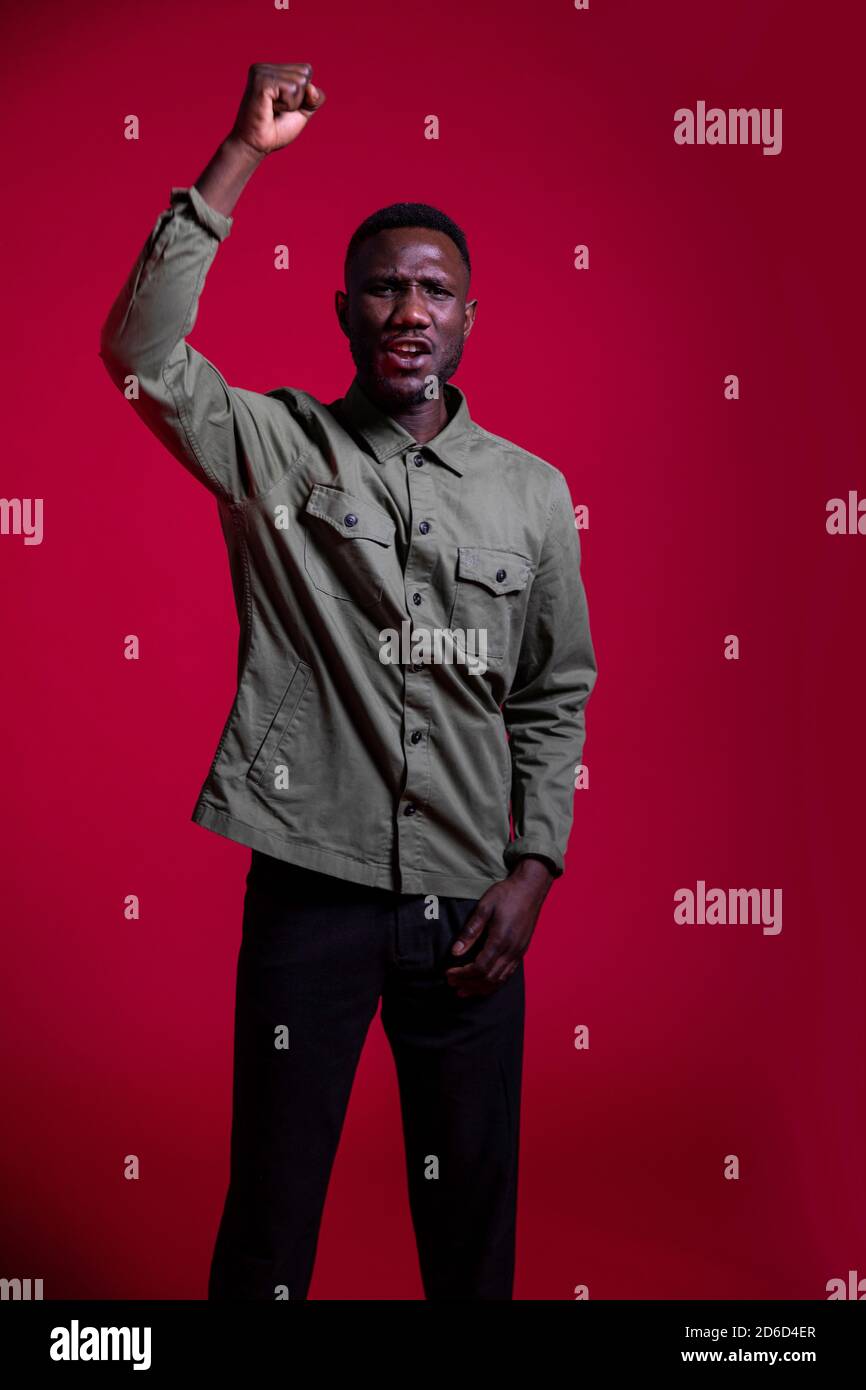 Junger schwarzer Mann, der aus Protest gegen professionelle Fotoshootings den Arm hebt. Isoliert. Dreiviertel Länge. Stockfoto