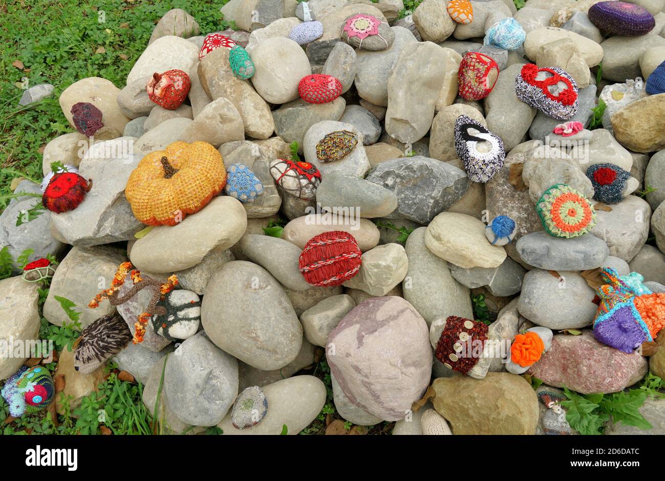 Ein Haufen von glatten ovalen Steinen. Einige von ihnen sind von gehäkelten Dekoration von verschiedenen Stilen und Farben bedeckt. Die kreative Idee macht die Steine einzigartig. Stockfoto