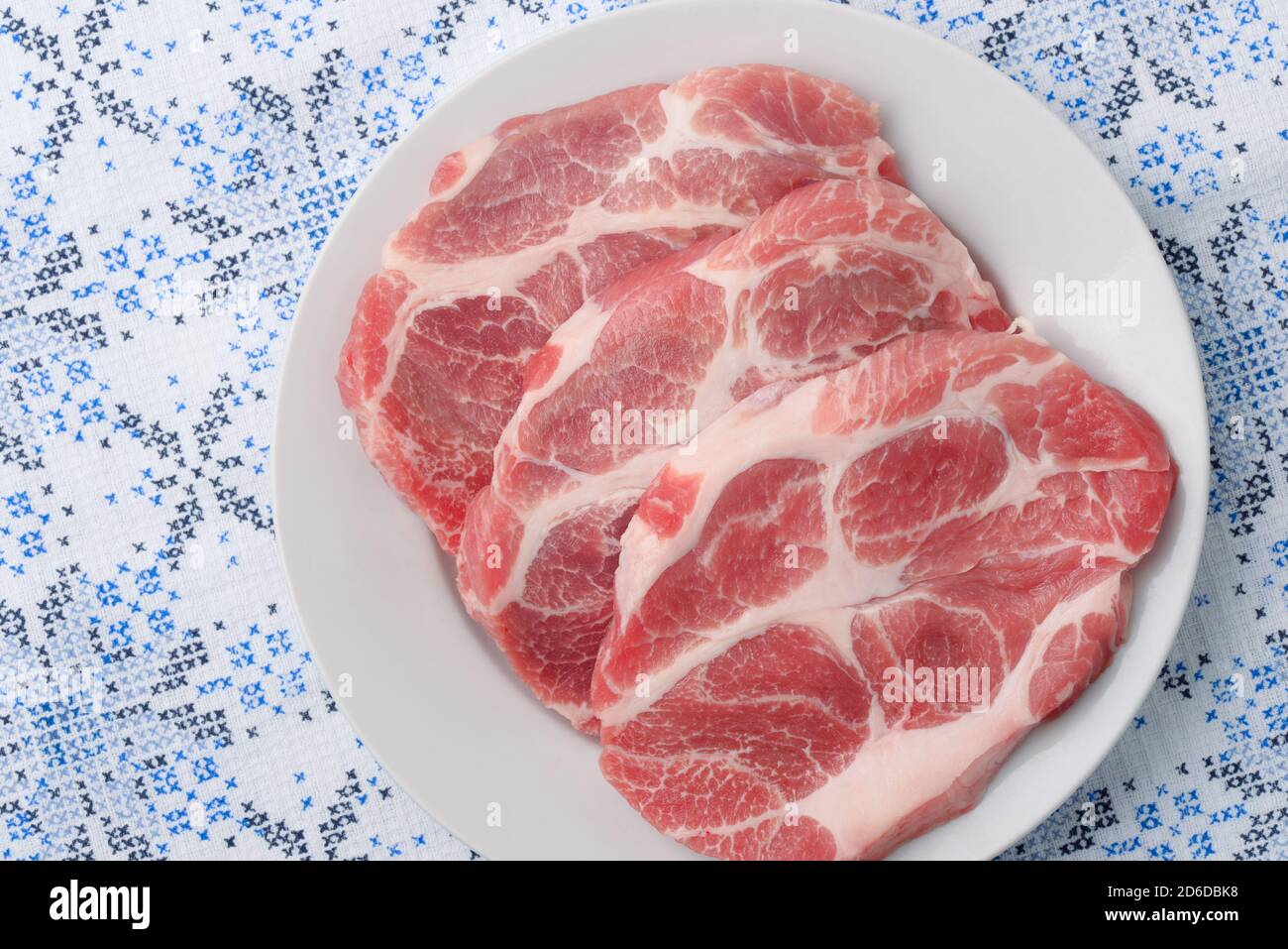 Draufsicht auf drei rohe, frische Schweinehals-Fleischsteaks Auf weißem Teller Stockfoto