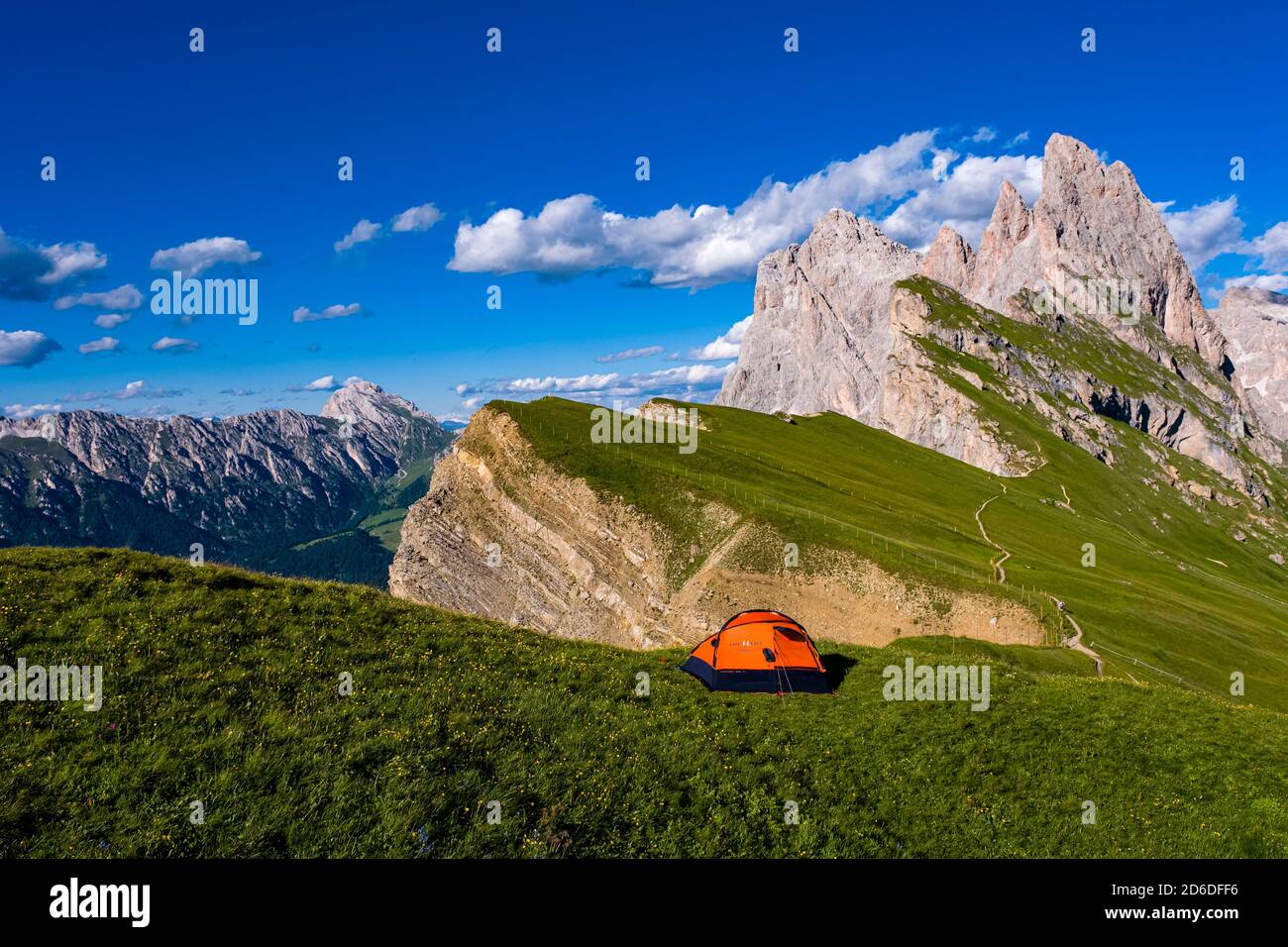 Ein orangefarbenes Zelt, das auf den Almen aufgestellt ist, die die steilen, rauen Klippen und Gipfel der Gebirgsformation Seceda umgeben, Secèda, Teil der Stockfoto
