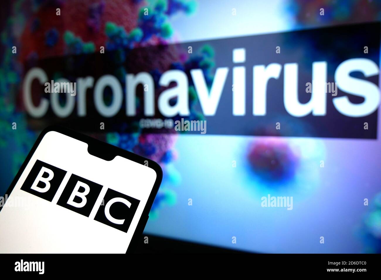 Das BBC-Logo auf einem Mobiltelefon mit einem illustrativen Modell des Coronavirus, das auf einem Monitor im Hintergrund angezeigt wird. Stockfoto