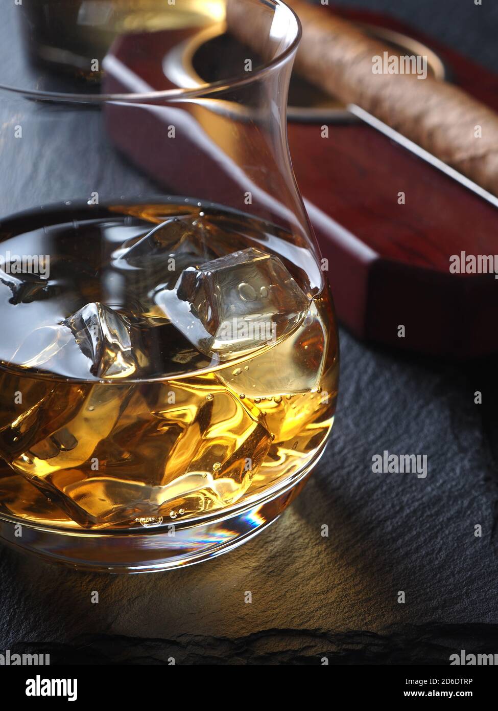 Whisky auf den Felsen und eine Zigarre in einem Aschenbecher Auf einer schwarzen Schieferfläche Stockfoto