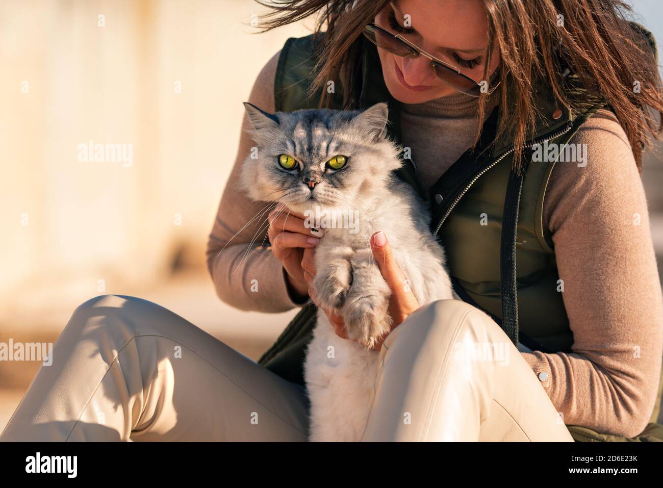Stilvolle Dame mit ihrer reinrassigen Katze sitzt draußen auf dem Sonnenuntergang. Haustier mit Eigentümer Stockfoto