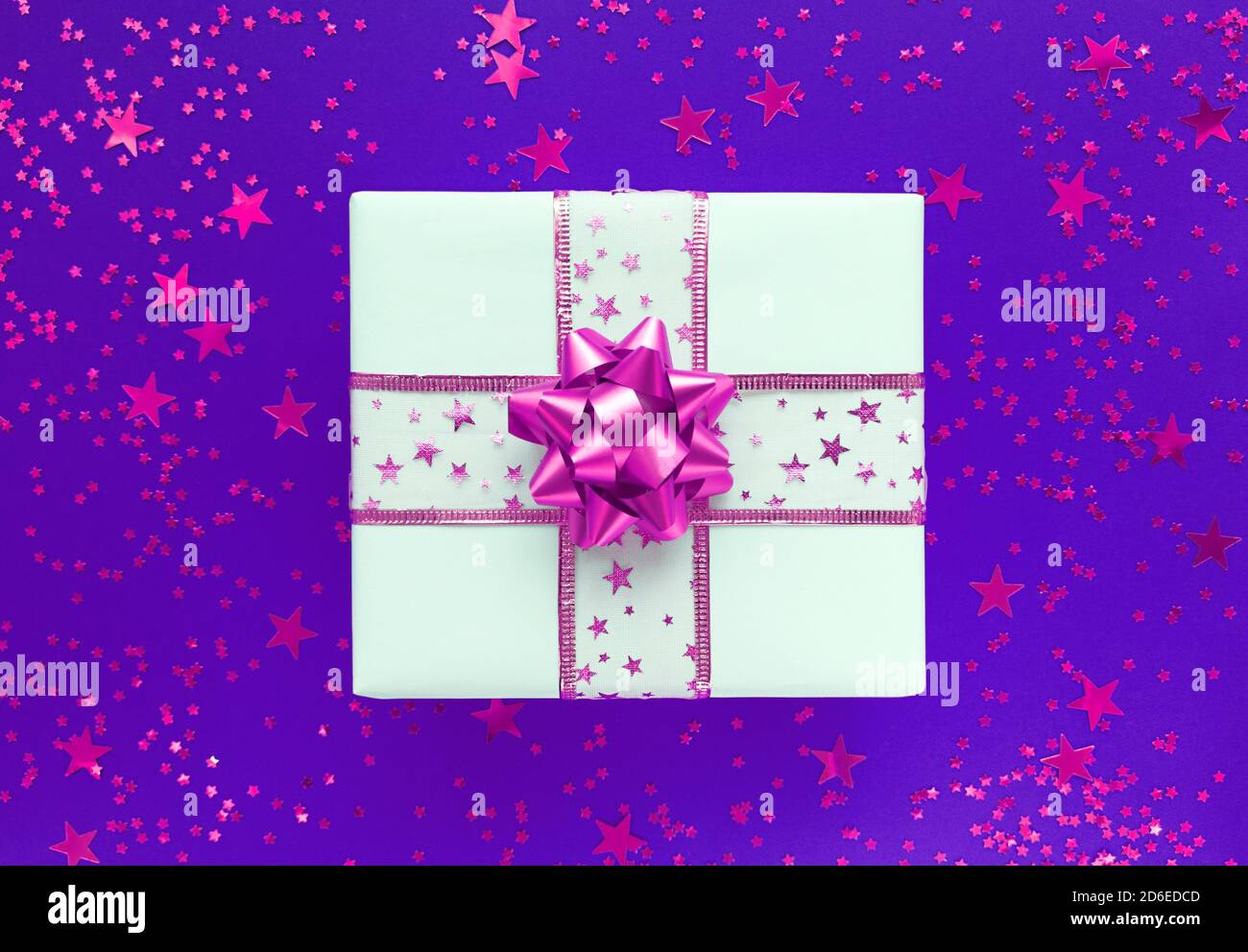 Weiße Geschenkbox mit rosa Schleife und Sternen auf violettem Hintergrund. Stockfoto