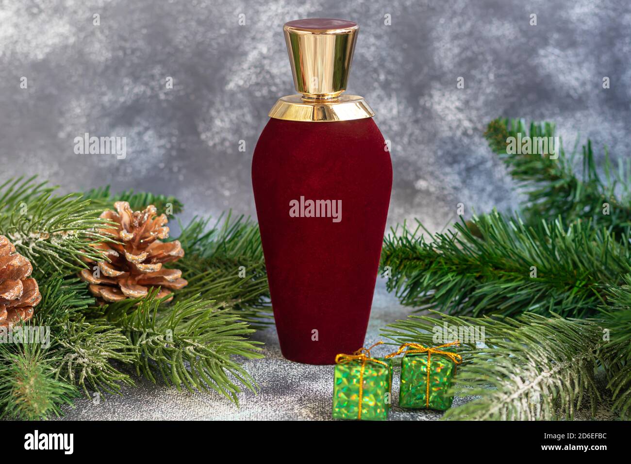 Parfümflasche. Umgeben von Christbaumzweigen und Weihnachtsspielzeug. Geschenkkonzept für Neujahr und Weihnachten. Auf einem hellen Hintergrund. Stockfoto